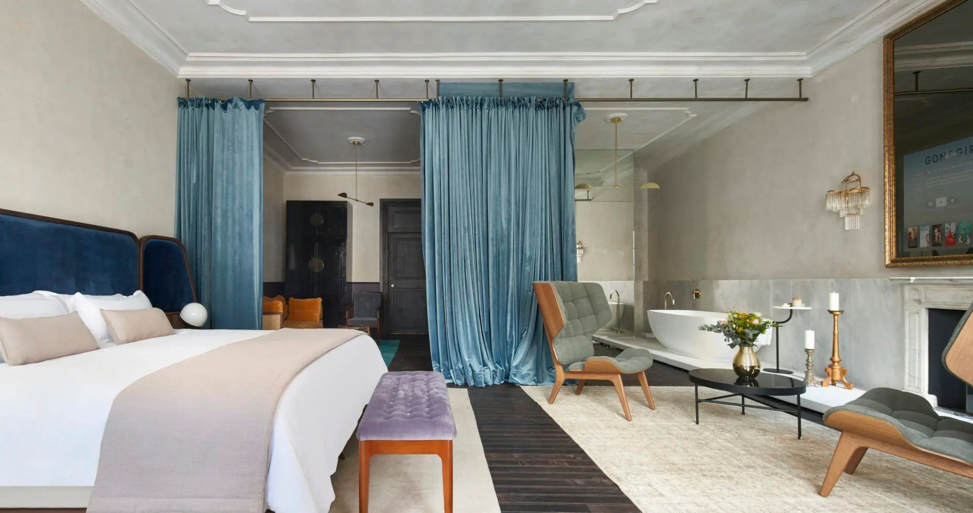 Schlafbereich einer Suite mit Doppelbett, blauen Vorhängen und einer freistehenden Badewanne.