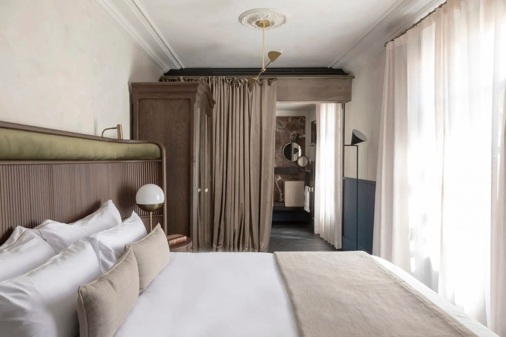 Schlafbereich mit weißem Bett und Vorhang, der zum angrenzenden Badezimmer führt.