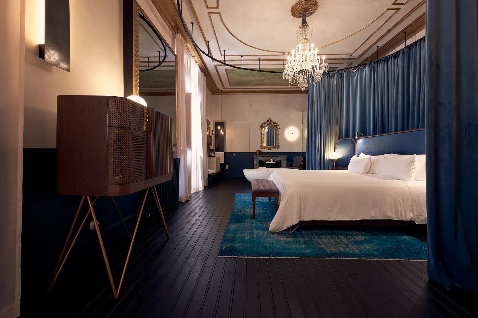 Geräumige Suite mit großem Bett, blauem Vorhang, Kronleuchter und dunklem Holzboden.