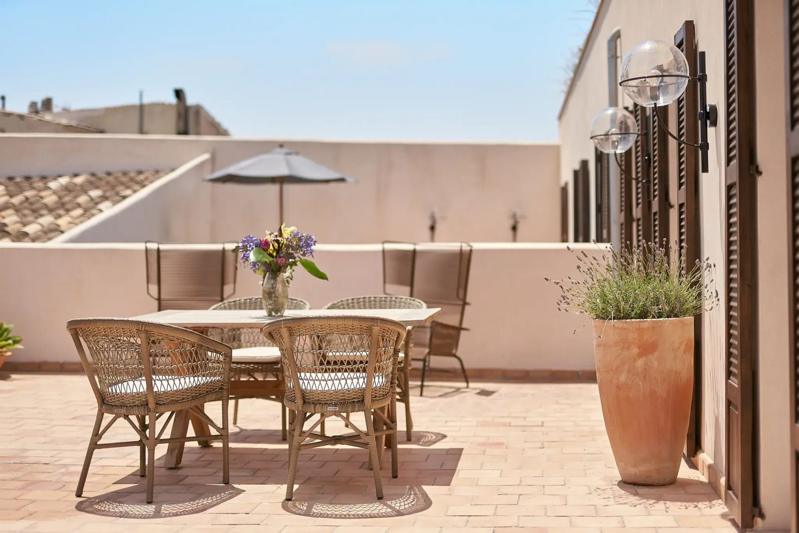 Sonnige Terrasse mit Esstisch aus Holz, Flechtstühlen und Blumenstrauß