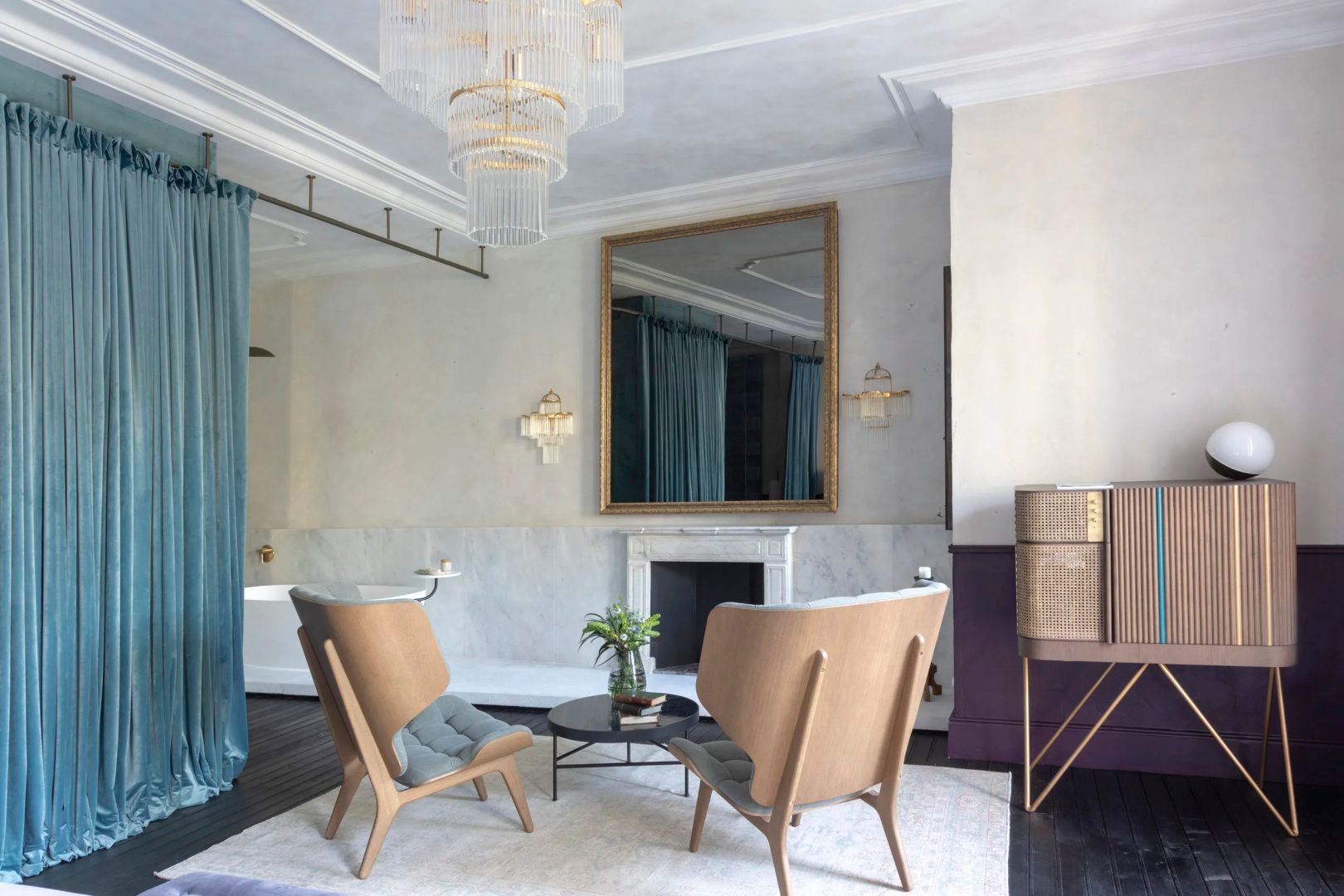 Sitzbereich in einer Suite mit zwei Sesseln, einem Kamin, einem großen Wandspiegel und Kronleuchter.