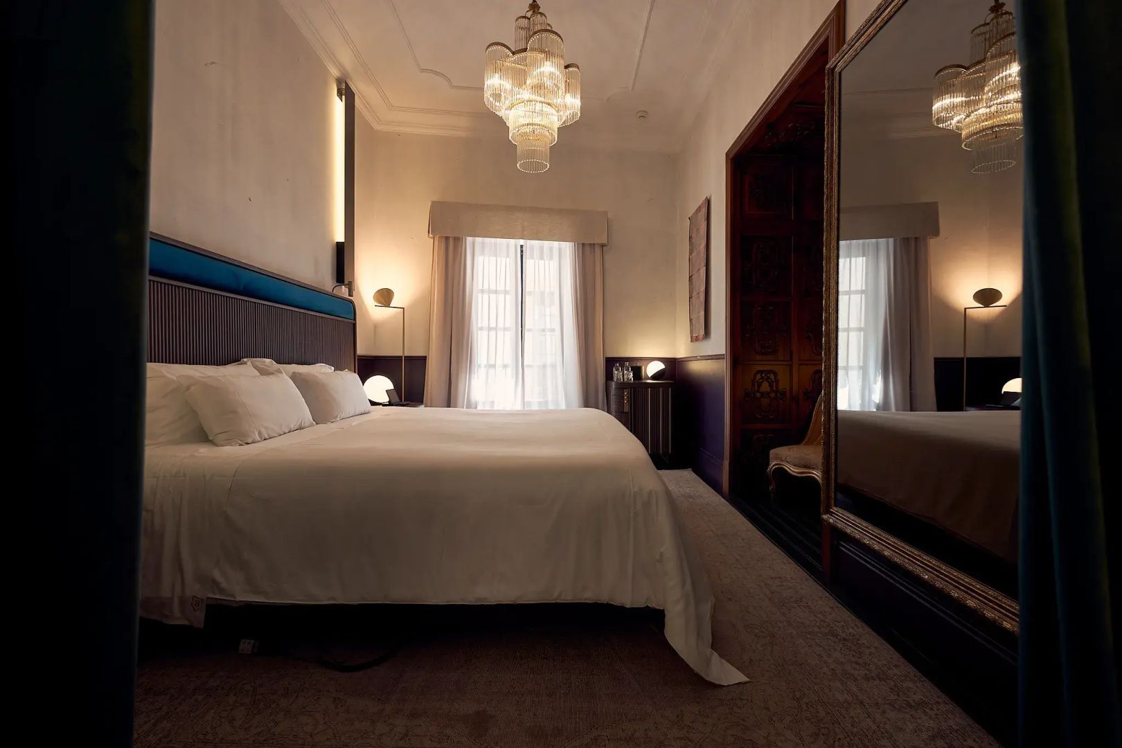 Zimmer mit großem Bett, Kronleuchter an der Decke und Stehspiegel an der Wand.