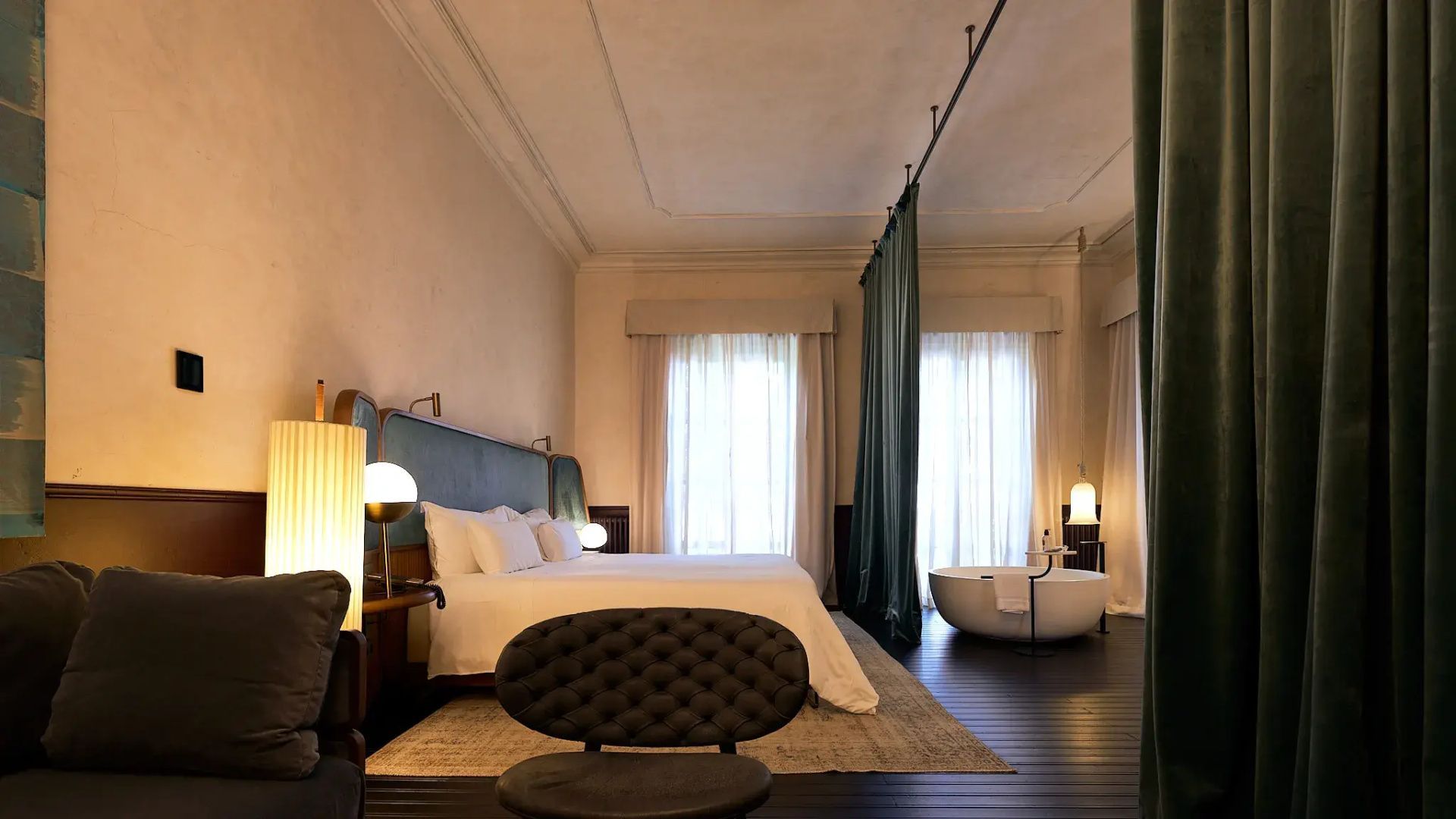 Hotelzimmer mit Doppelbett, grünem Raumteiler Vorhang und freistehender Badewanne.