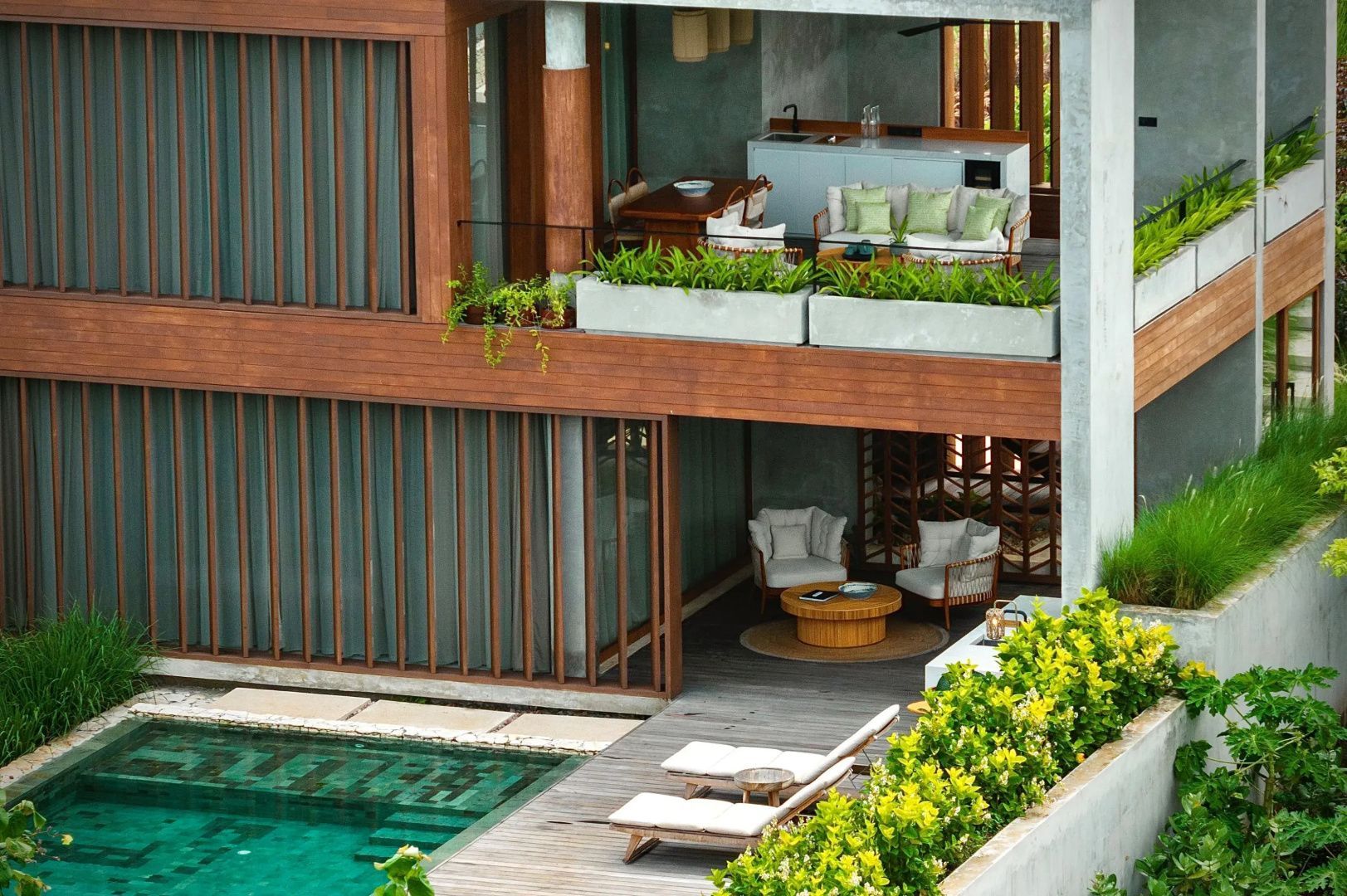 Zweigeschossiges Gebäude mit Balkon, Terrasse, Sitzmöbeln und einem Pool davor.