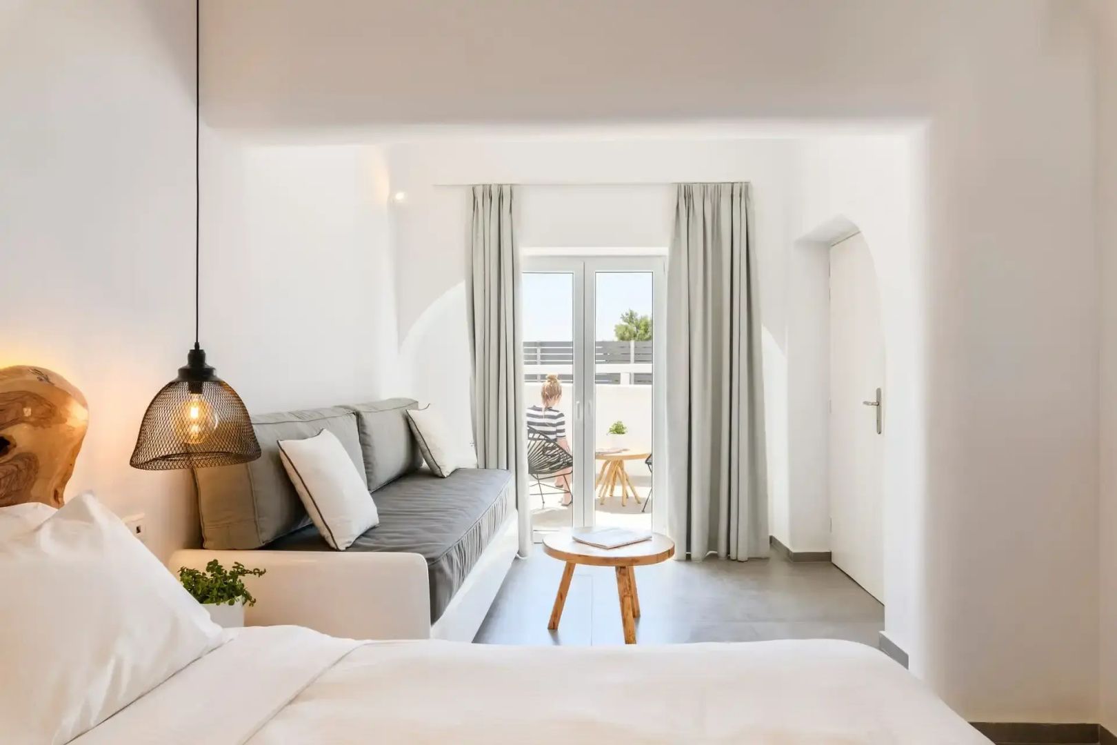 Helles Hotelzimmer mit grauem Sofa, kleinem Holztisch und Blick auf die Terrasse.