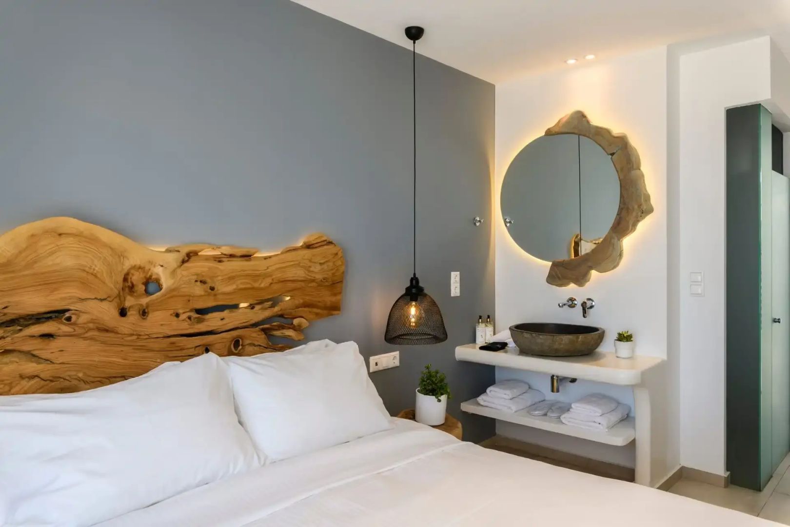 Doppelbett mit hölzernem Kopfteil neben einem Waschtisch mit beleuchtetem Rundspiegel.