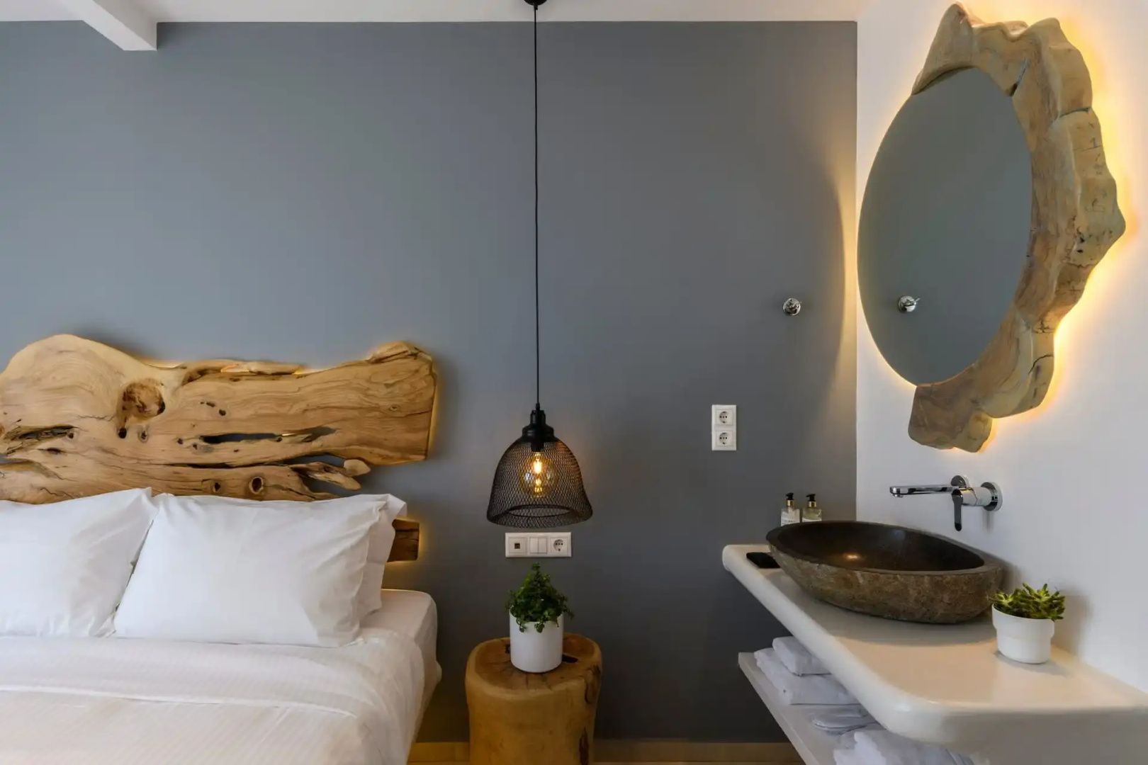 Bett mit Kopfteil aus Naturholz, hängender Lampe und angrenzendem Waschbecken.