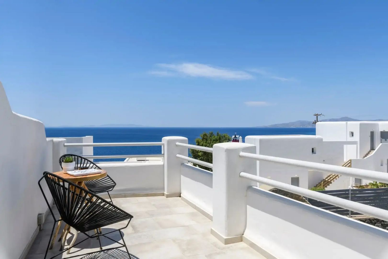 Weiße Terrasse mit schwarzen Stühlen und Blick auf das tiefblaue Meer.