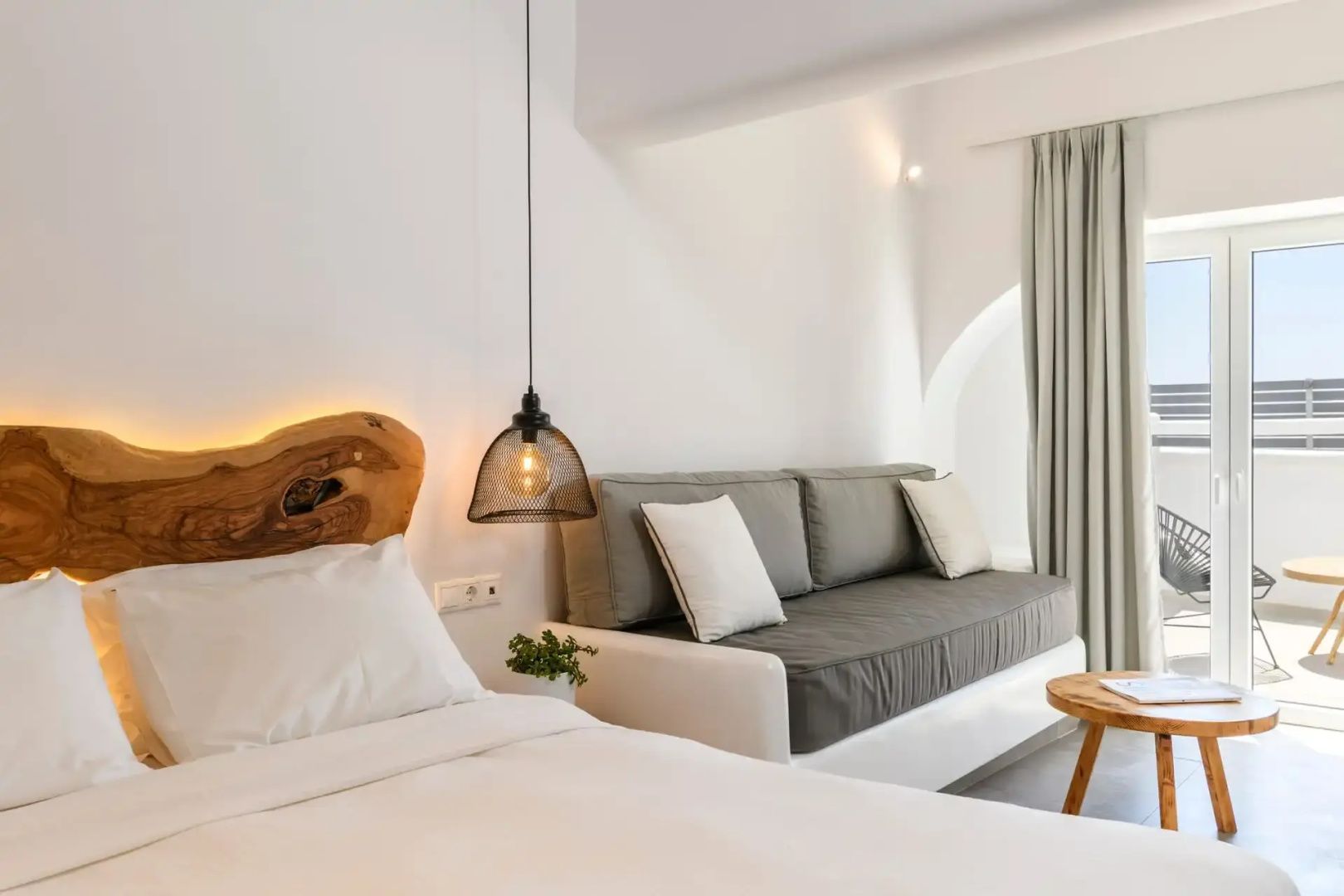 Schlaf- und Wohnbereich mit weißem Bett, grauem Sofa und stilvoller Hängelampe.
