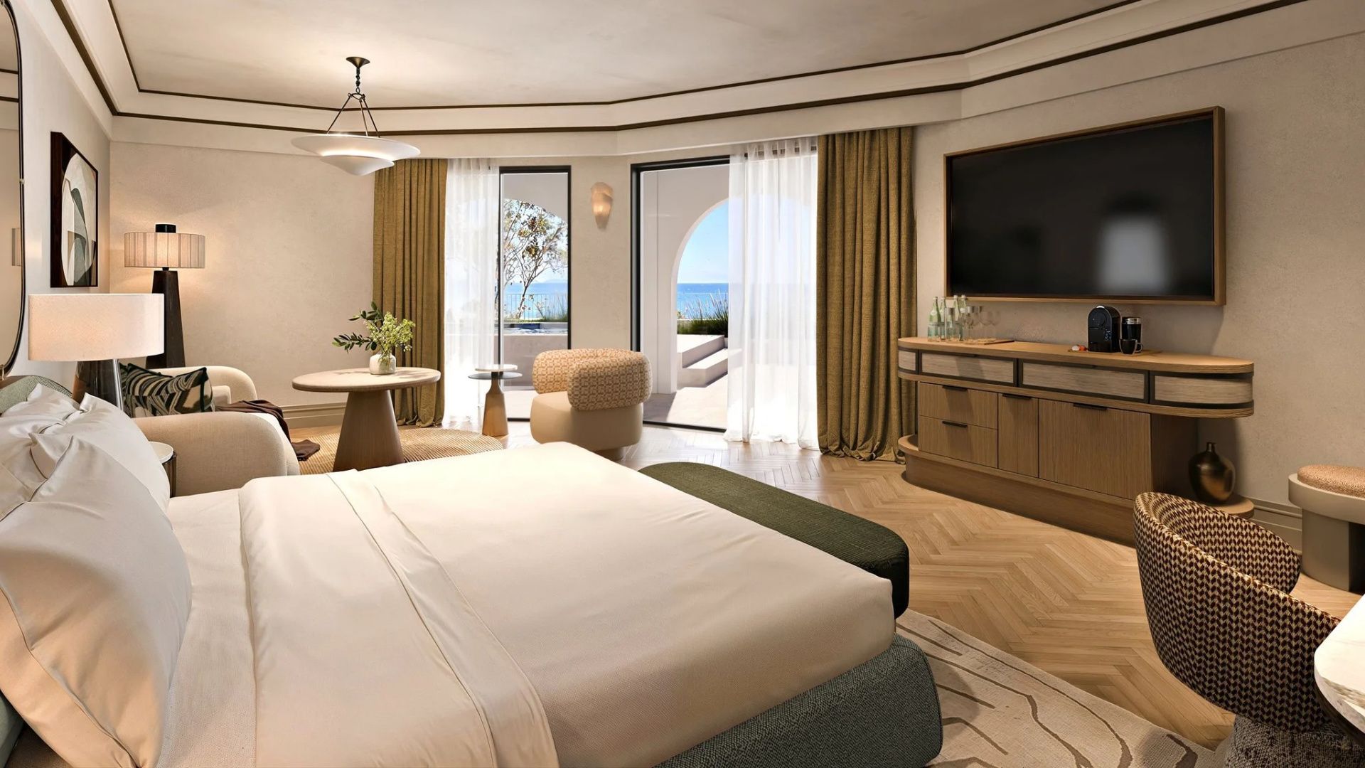 Helles Schlafzimmer einer Suite mit Doppelbett, Sitzbereich und Blick durch große Türen auf das Meer.