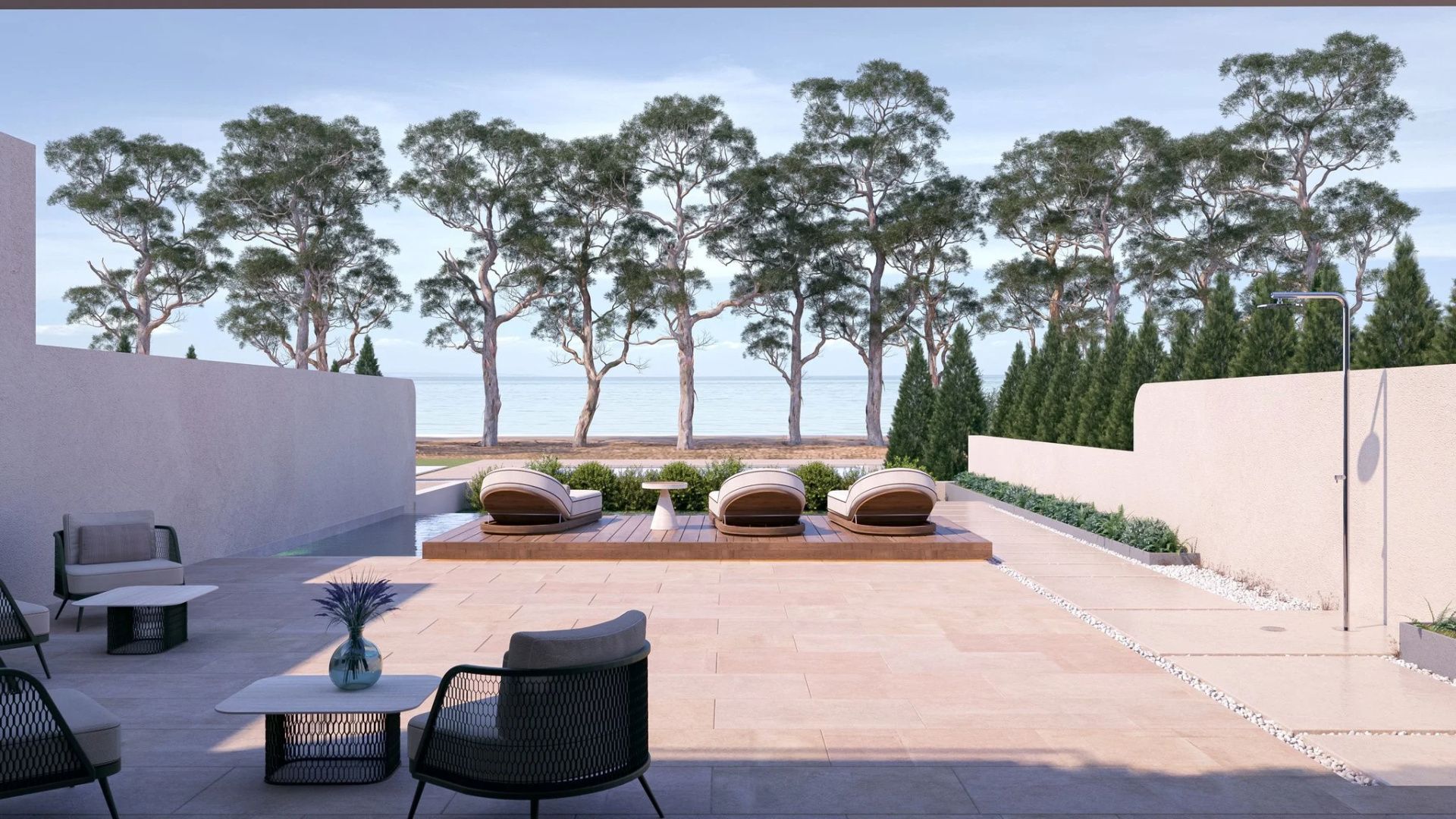 Sonnenterrasse mit Liegestühlen und Blick über einen Pool hin zum Meer hinter hohen Bäumen.