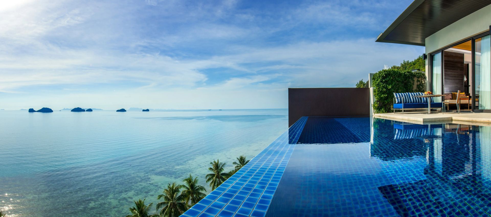 Blau gefliester Infinity Pool mit Blick auf das ruhige Meer und grüne Palmen.