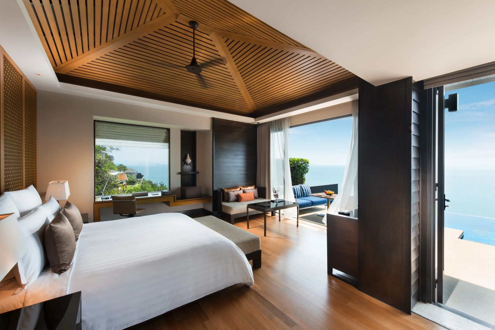 Schlafzimmer mit großem Bett, Holzboden und offenem Zugang zur Terrasse am Meer.