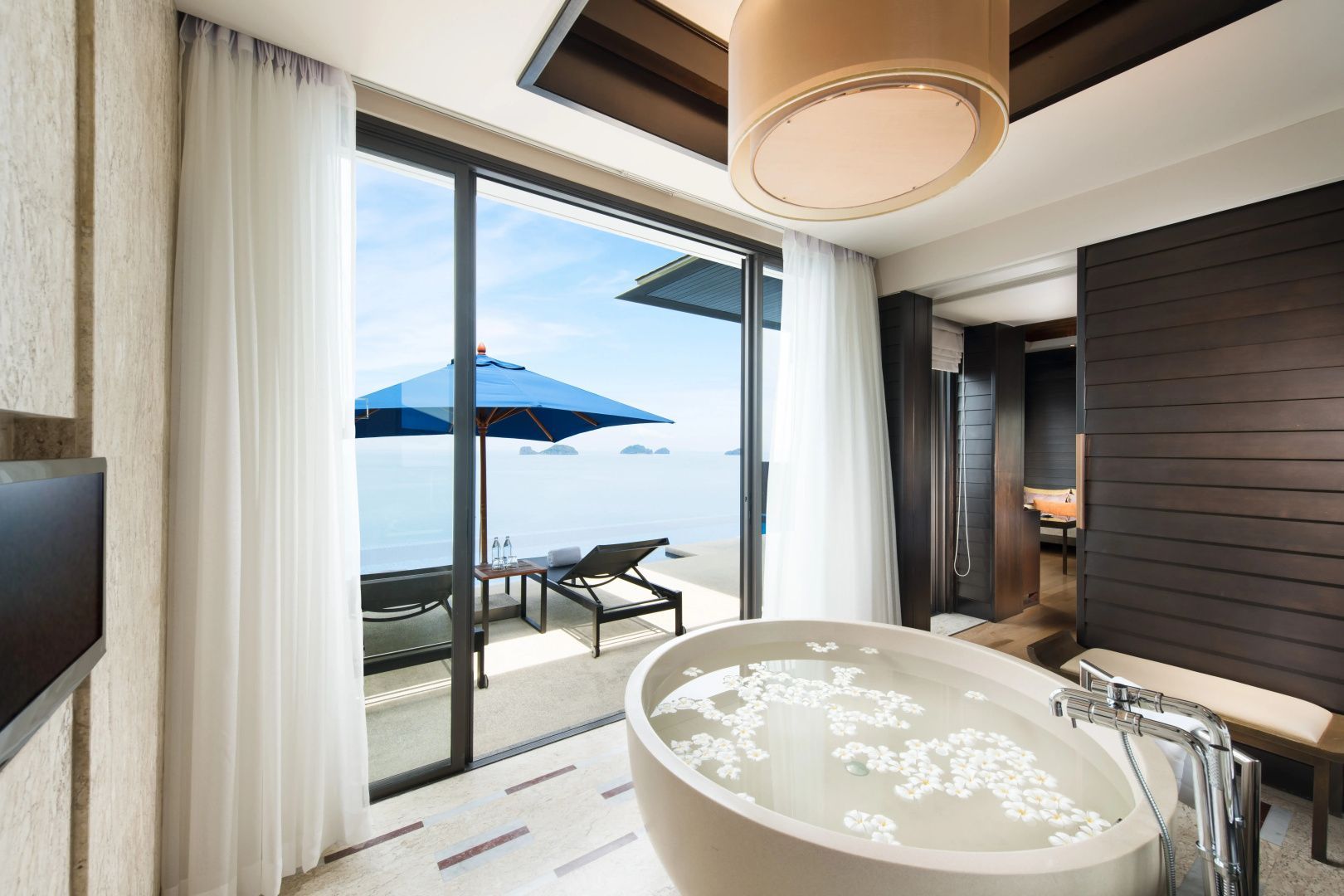 Freistehende runde Badewanne mit Blüten im Badezimmer mit Sicht auf das Meer.