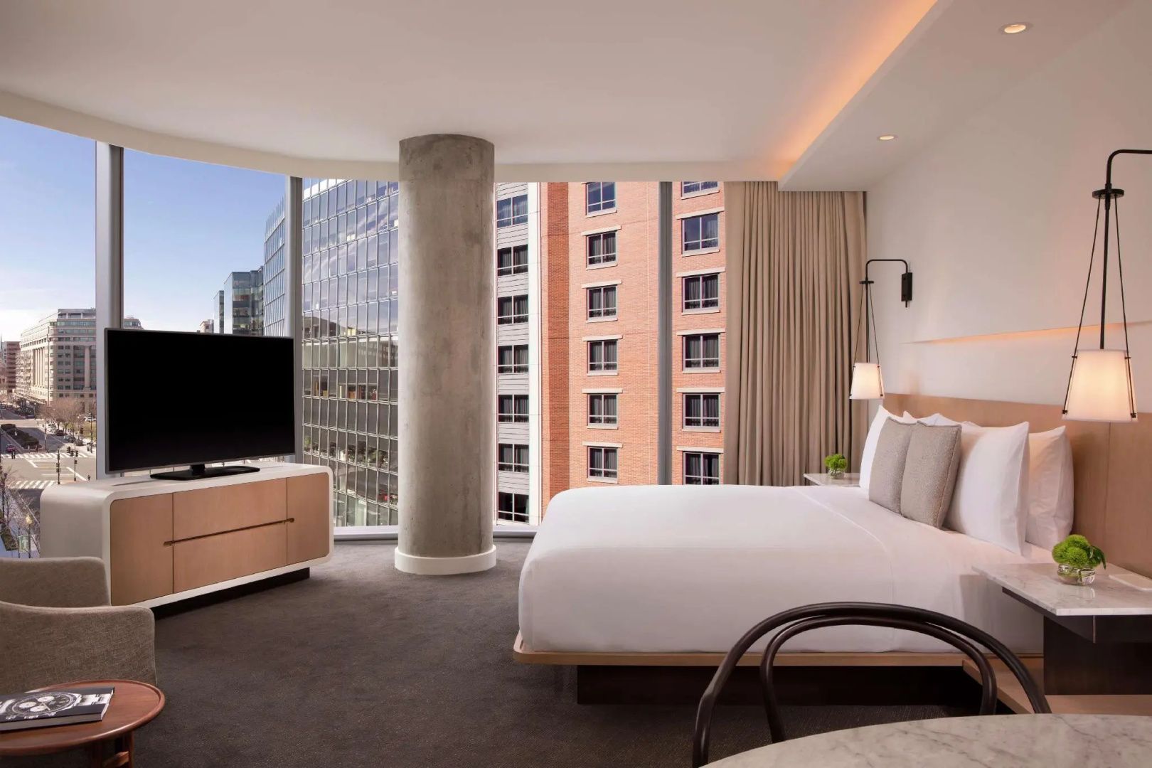 Helles Hotelzimmer mit Doppelbett, Säule und Ausblick auf Stadtgebäude.