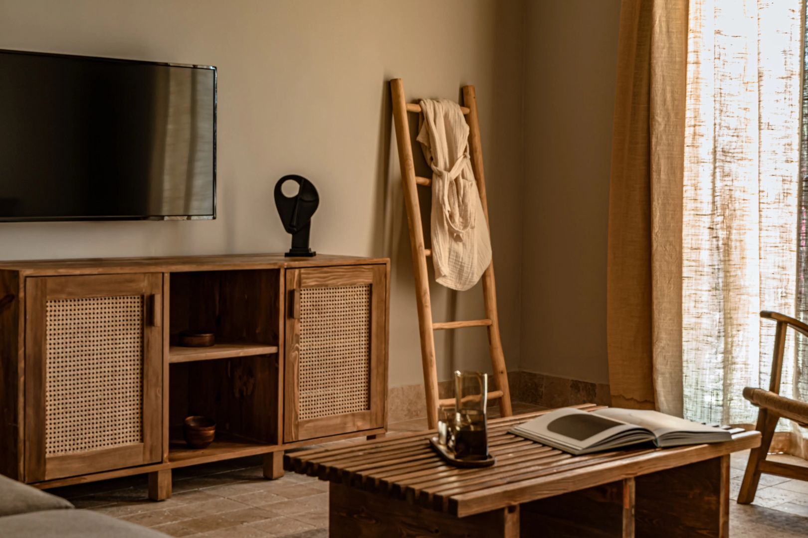 Holzkommode mit Fernseher und eine lehnende Holzleiter mit Bademantel im Zimmer.