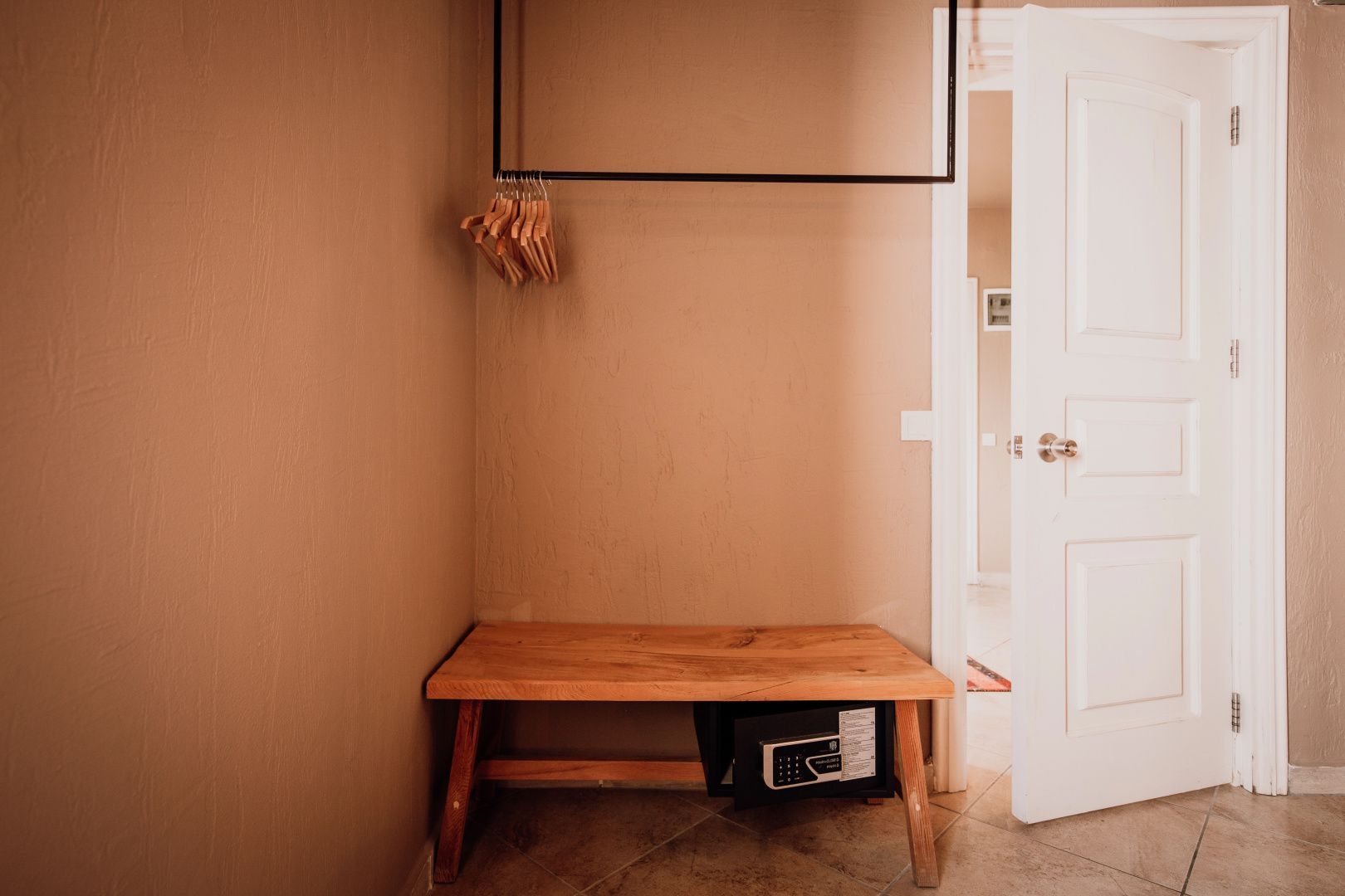 Holzbank mit eingebautem Safe im Zimmer sowie offener Kleiderstange mit Bügeln.