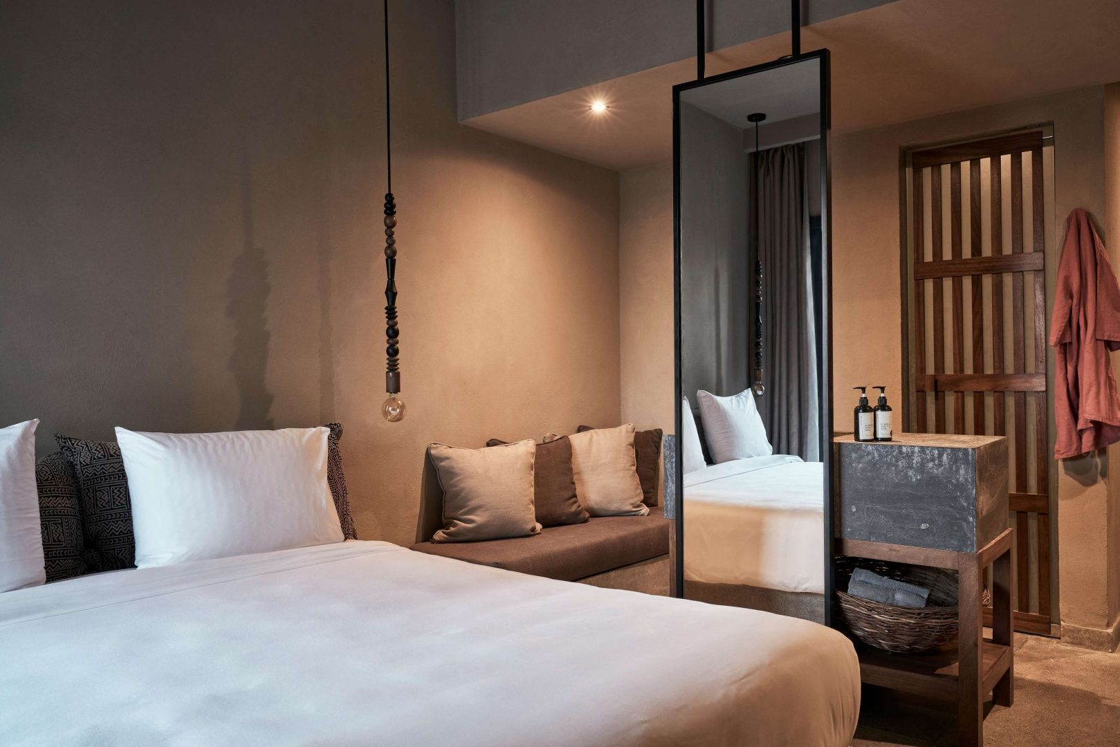 Modernes Hotelzimmer mit Bett, Sitzbank mit Kissen und einem großen Standspiegel.