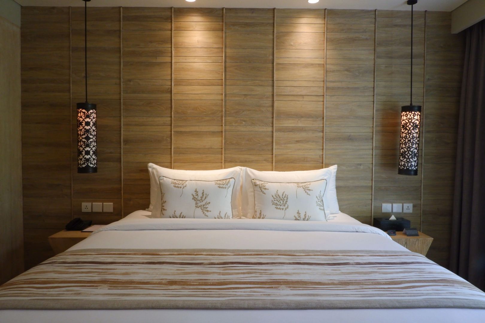 Doppelbett mit weißer Bettwäsche und hölzerner Wandverkleidung im Hotelzimmer.