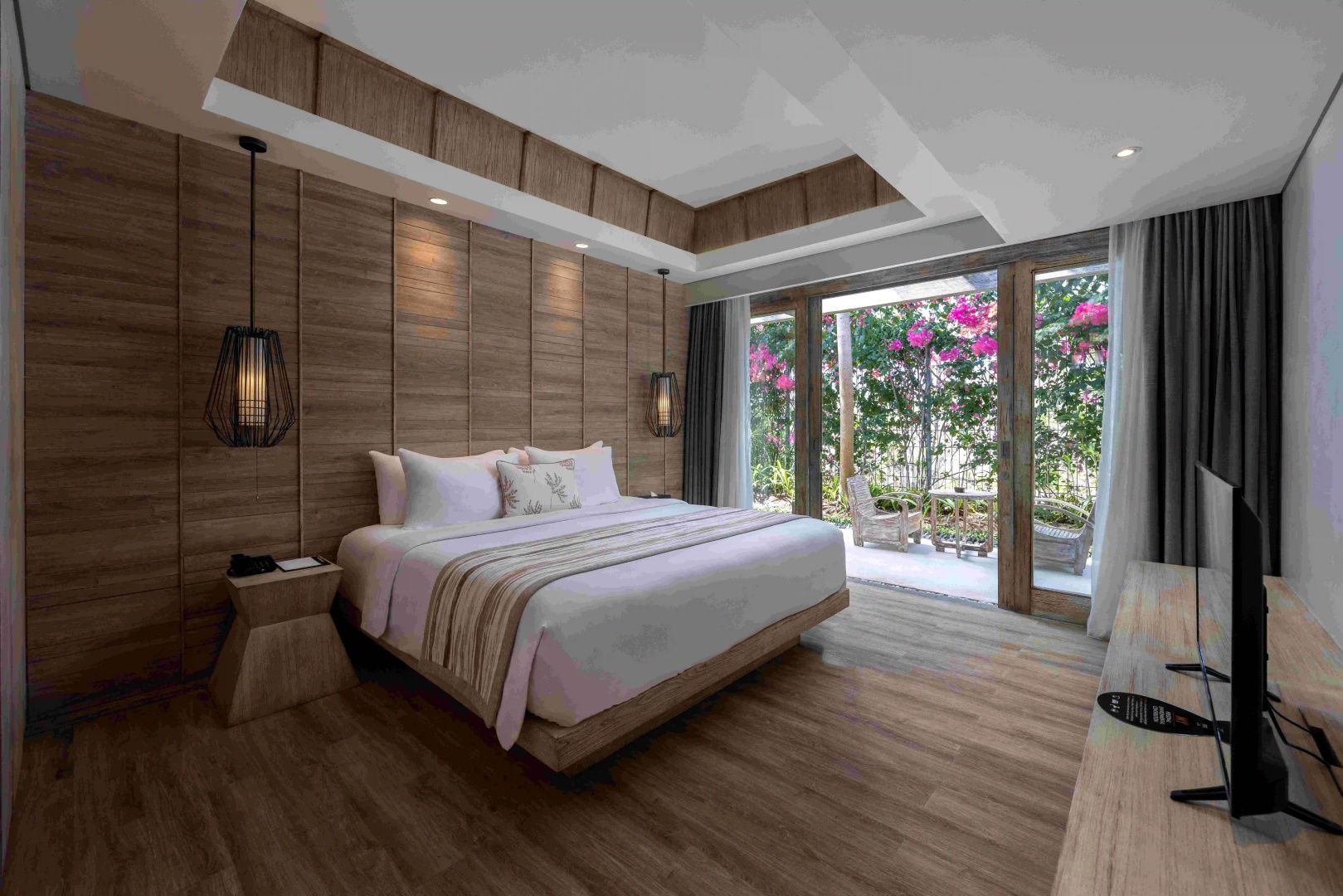 Geräumiges Hotelzimmer mit großem Doppelbett und Zugang zur begrünten Terrasse.