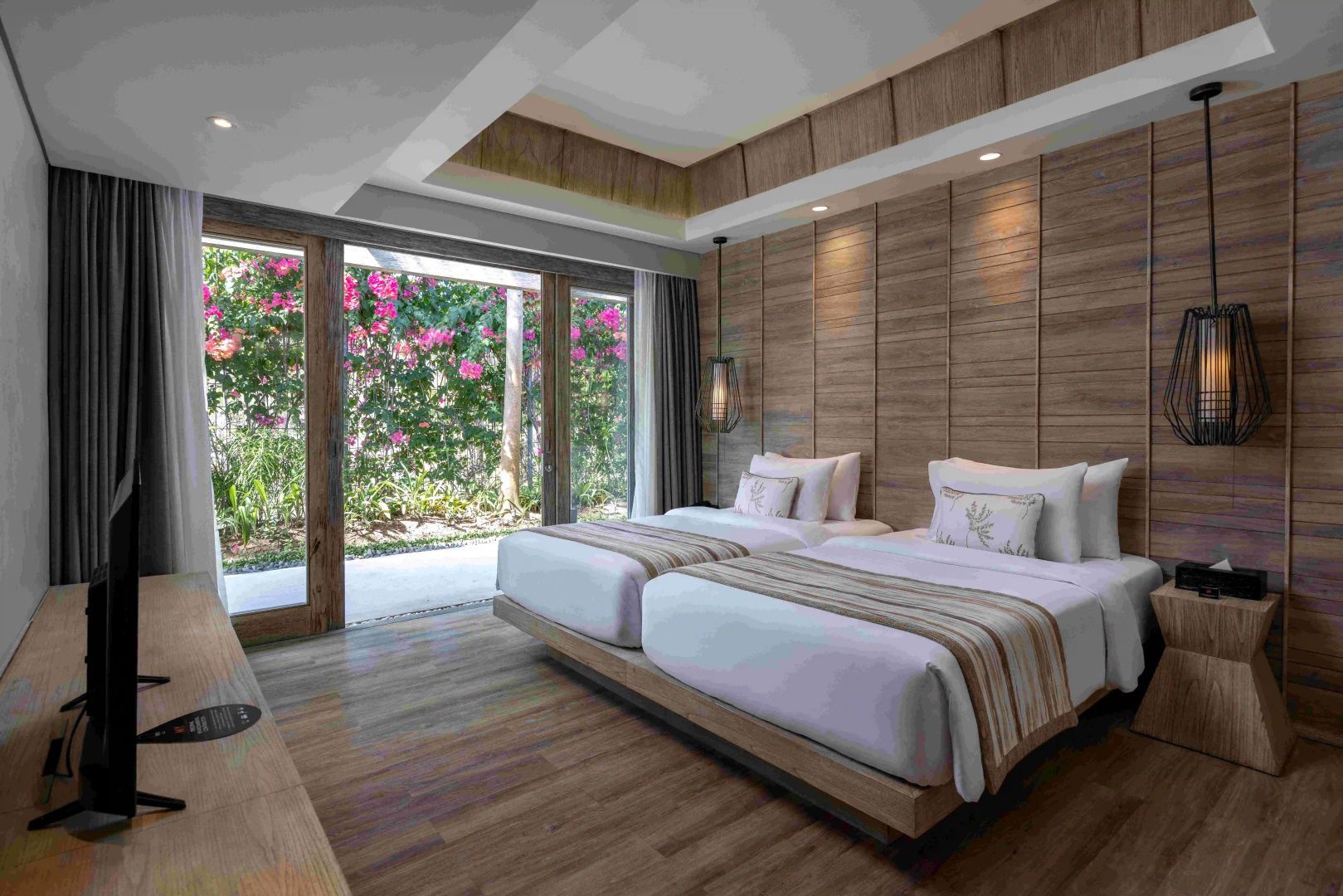 Schlafzimmer mit zwei Einzelbetten, Holzdekor und Blick auf den blühenden Garten.