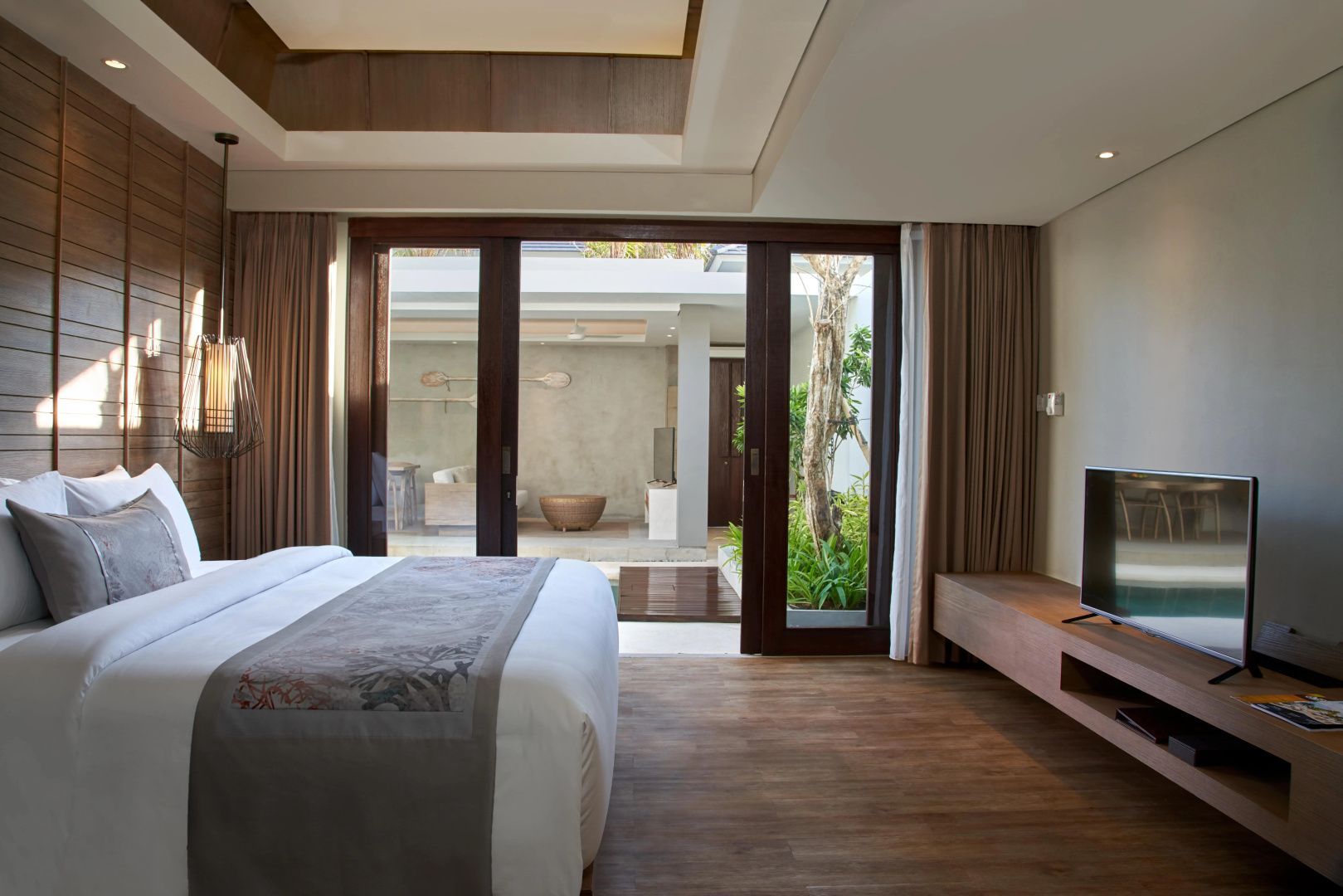 Hotelzimmer mit Doppelbett und Blick durch Schiebetüren auf eine überdachte Terrasse und Garten.