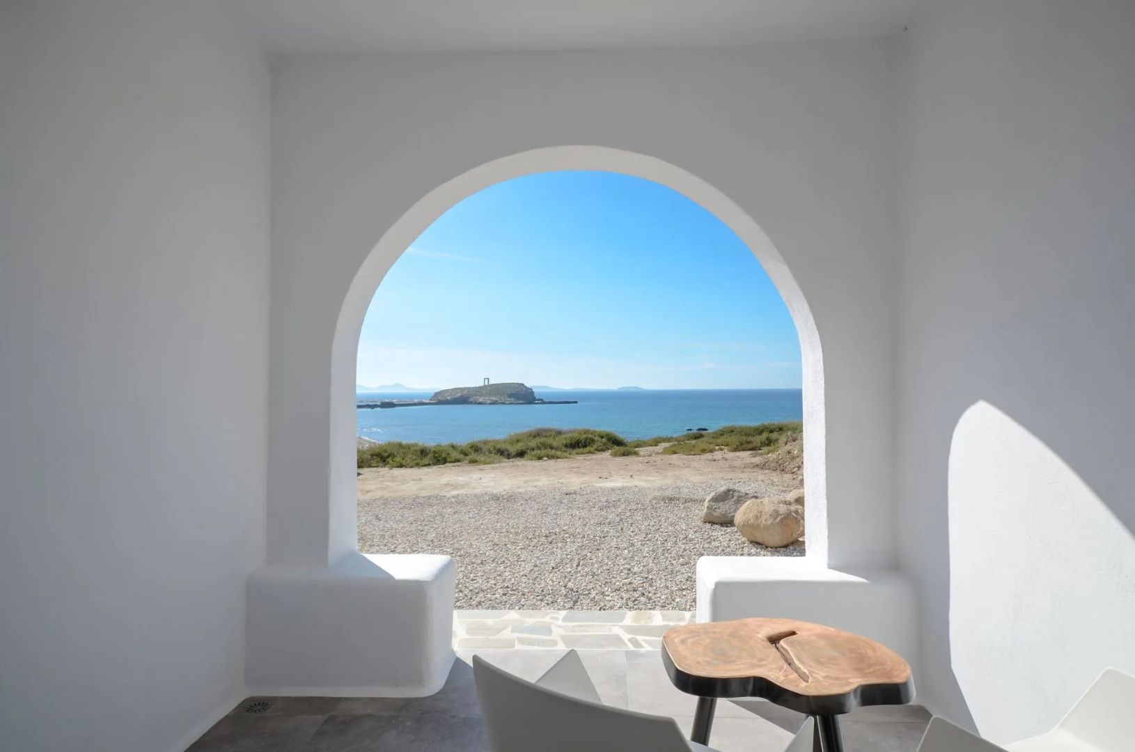 Blick durch einen Rundbogen auf eine Terrasse und das blaue Meer mit einer Insel.