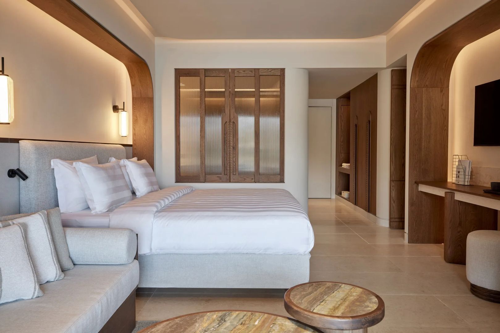 Großes Bett im hell eingerichteten Hotelzimmer mit Holzelementen an der Wand.