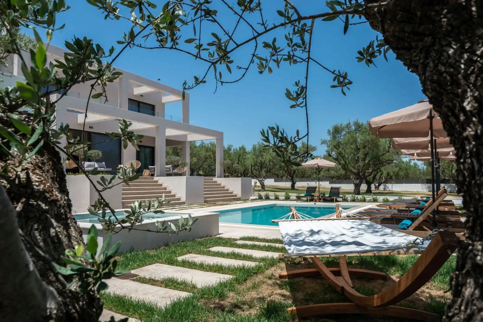 Moderne zweistöckige Villa mit hellen Treppen, Pool und Gartenbereich unter blauem Himmel.