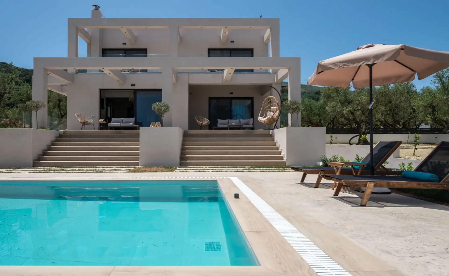 Rechteckiger Swimmingpool mit Liegestühlen im Außenbereich vor der modernen hellen Villa.
