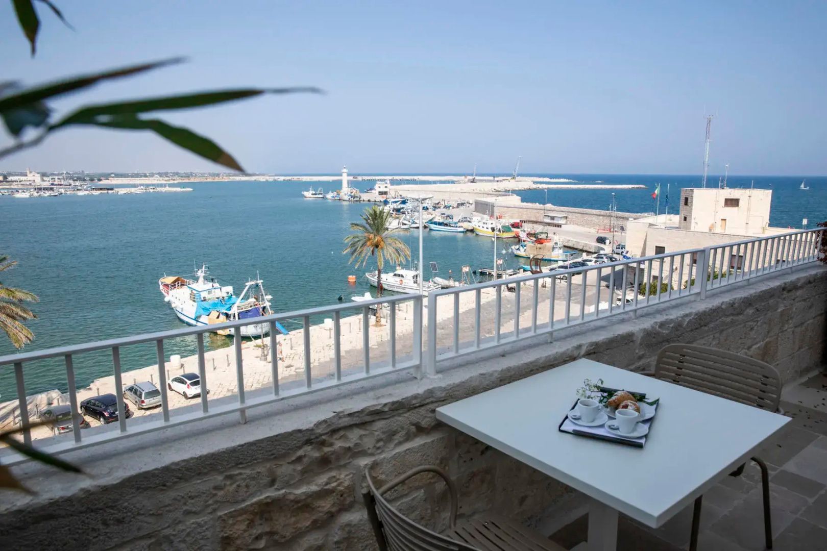 Blick von einem Balkon mit weißem Geländer und Frühstückstisch auf den Hafen mit Booten.