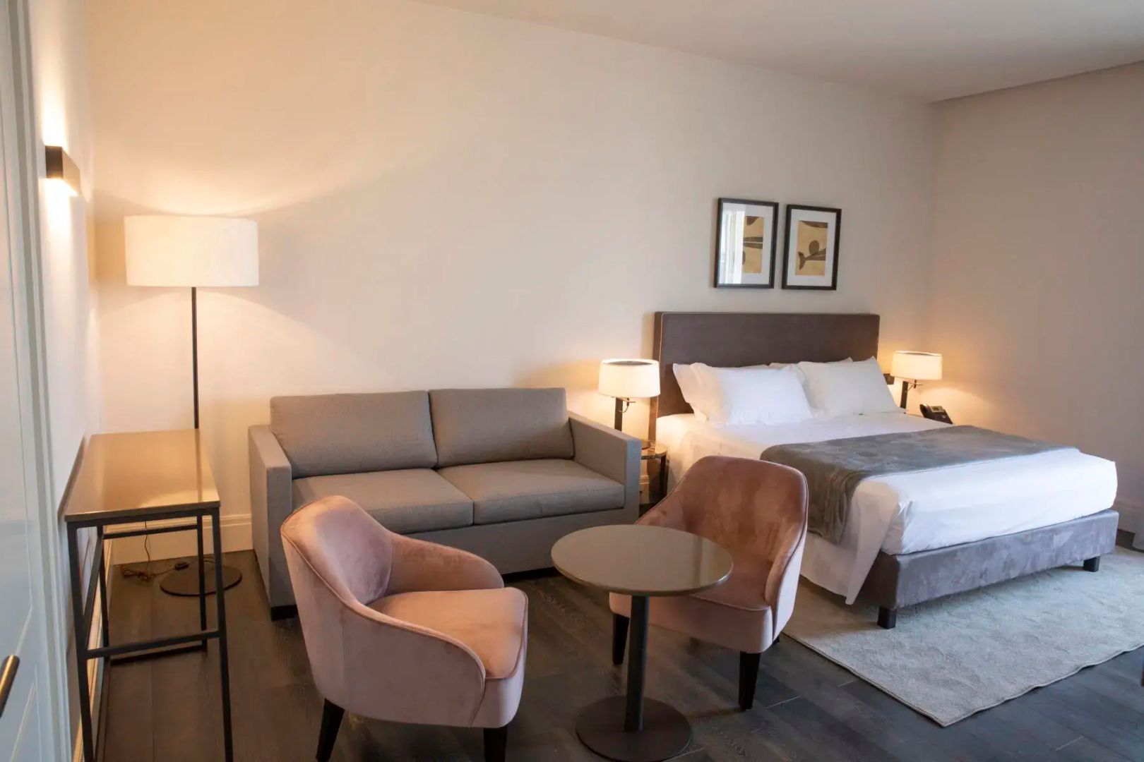 Hotelzimmer mit Doppelbett, grauem Sofa, zwei Sesseln und einem kleinen Tisch.