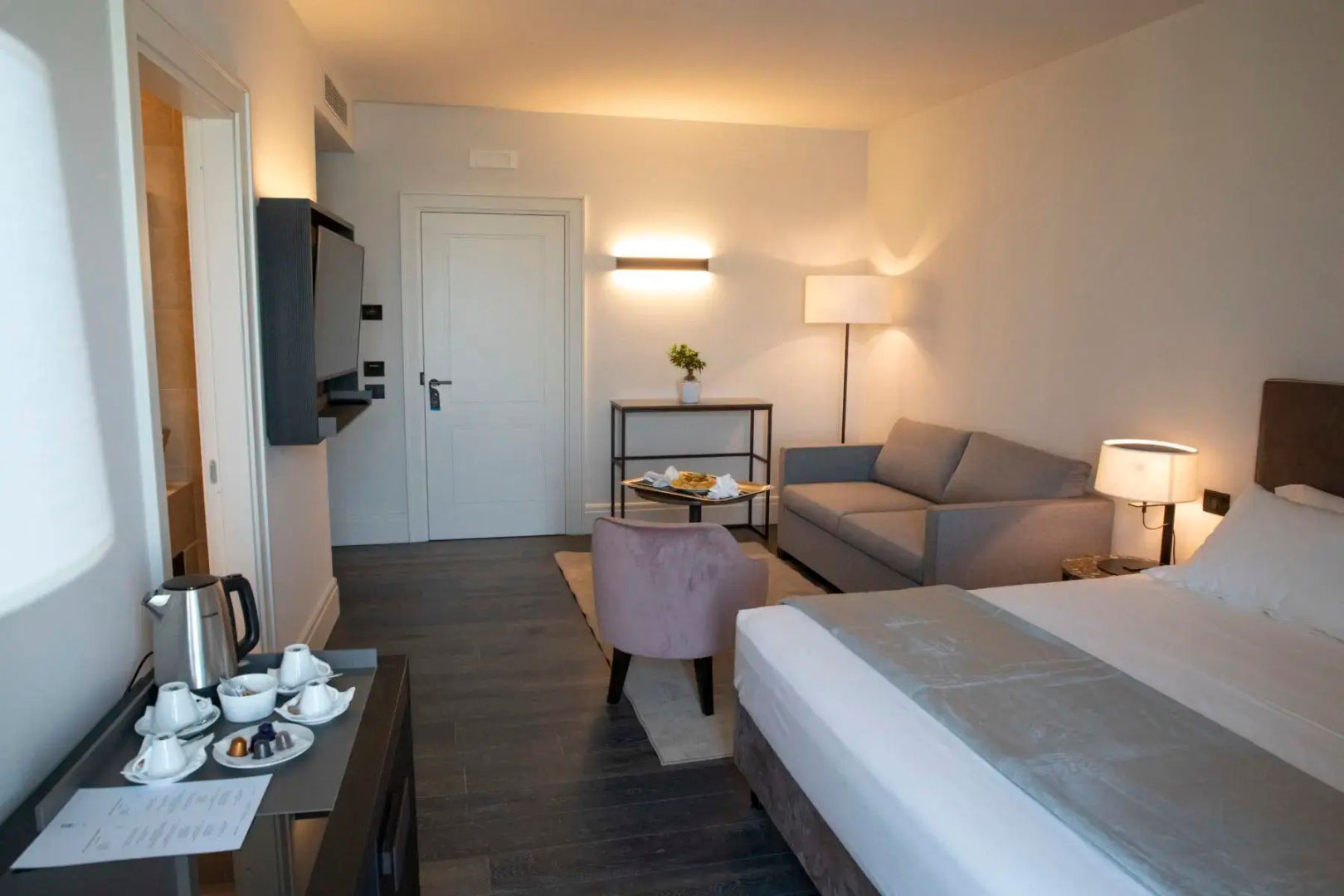 Geräumiges Hotelzimmer mit Flachbild-TV, Sofa, Sitzecke und weißer Eingangstür.