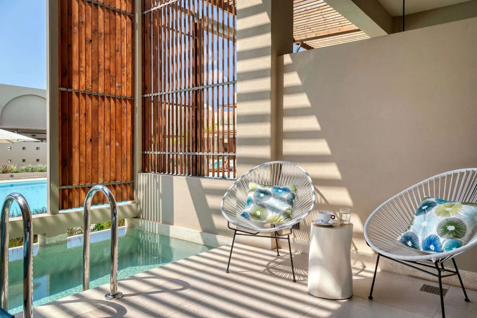 Sonnige Terrasse mit zwei Stühlen, Beistelltisch und Zugang zu einem kleinen Pool.