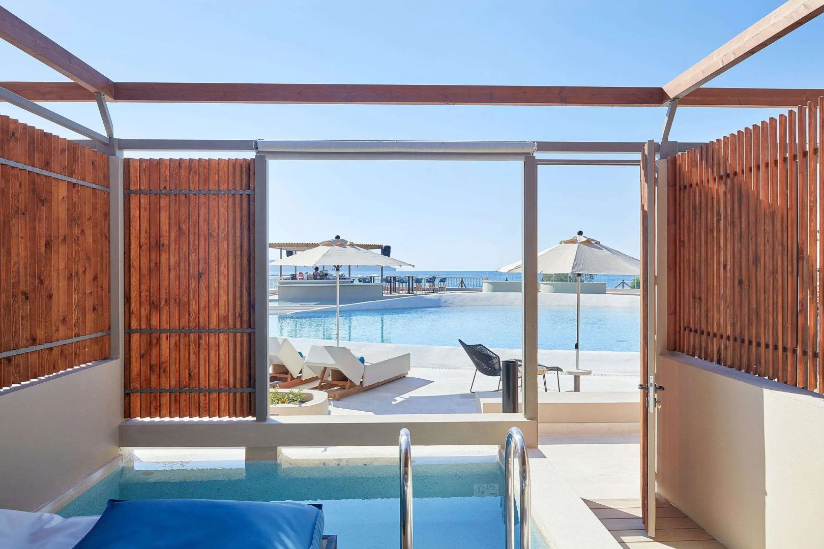 Terrasse mit kleinem Pool und Blick auf den Hauptpool, Sonnenschirme und das Meer.
