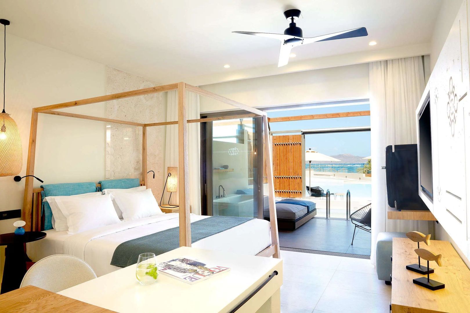 Modernes Hotelzimmer mit Holzhimmelbett, Deckenventilator und Schiebetür zur Terrasse mit Poolblick.