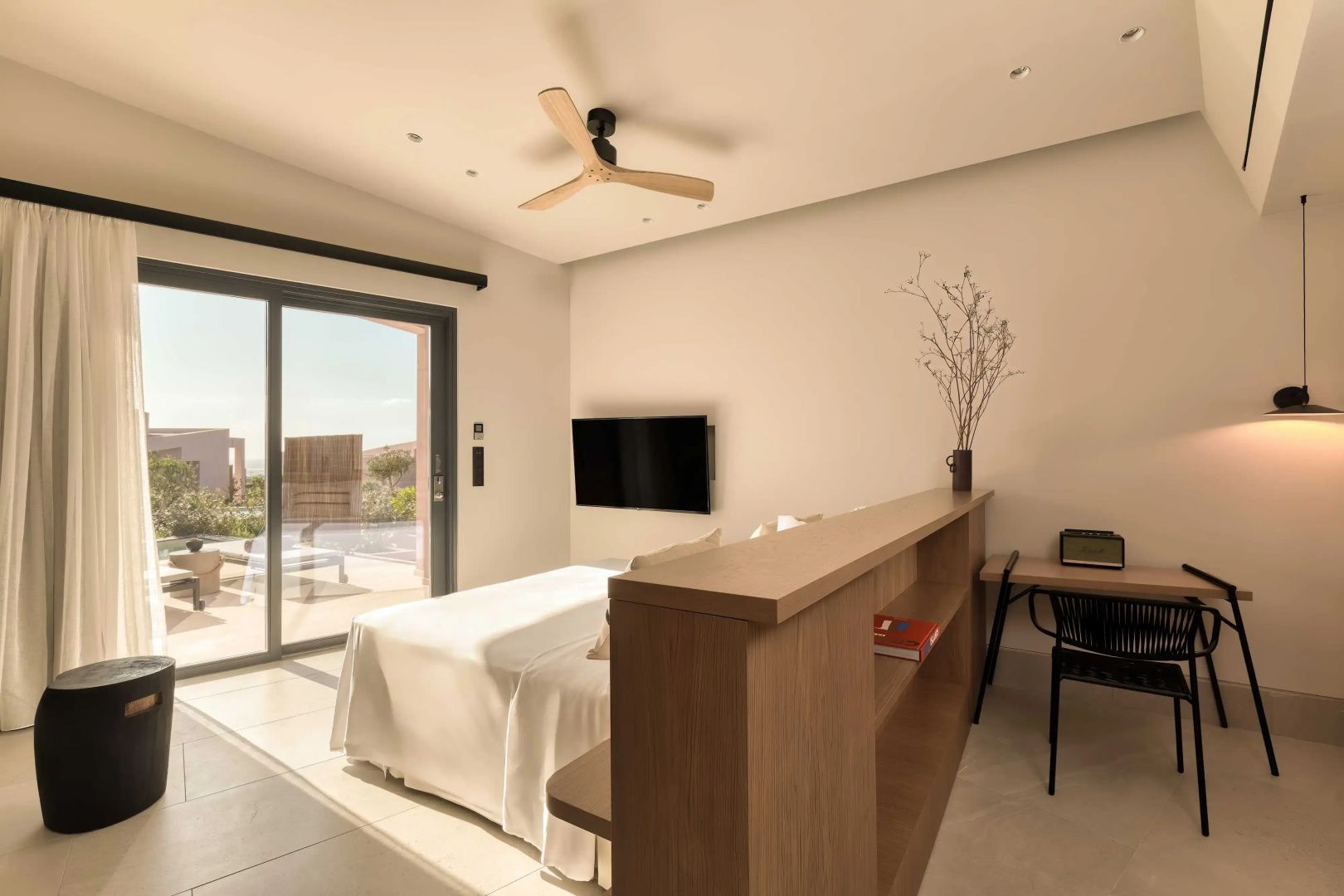 Helles Hotelzimmer mit Doppelbett, Deckenventilator, TV an der Wand und Zugang zur Terrasse.