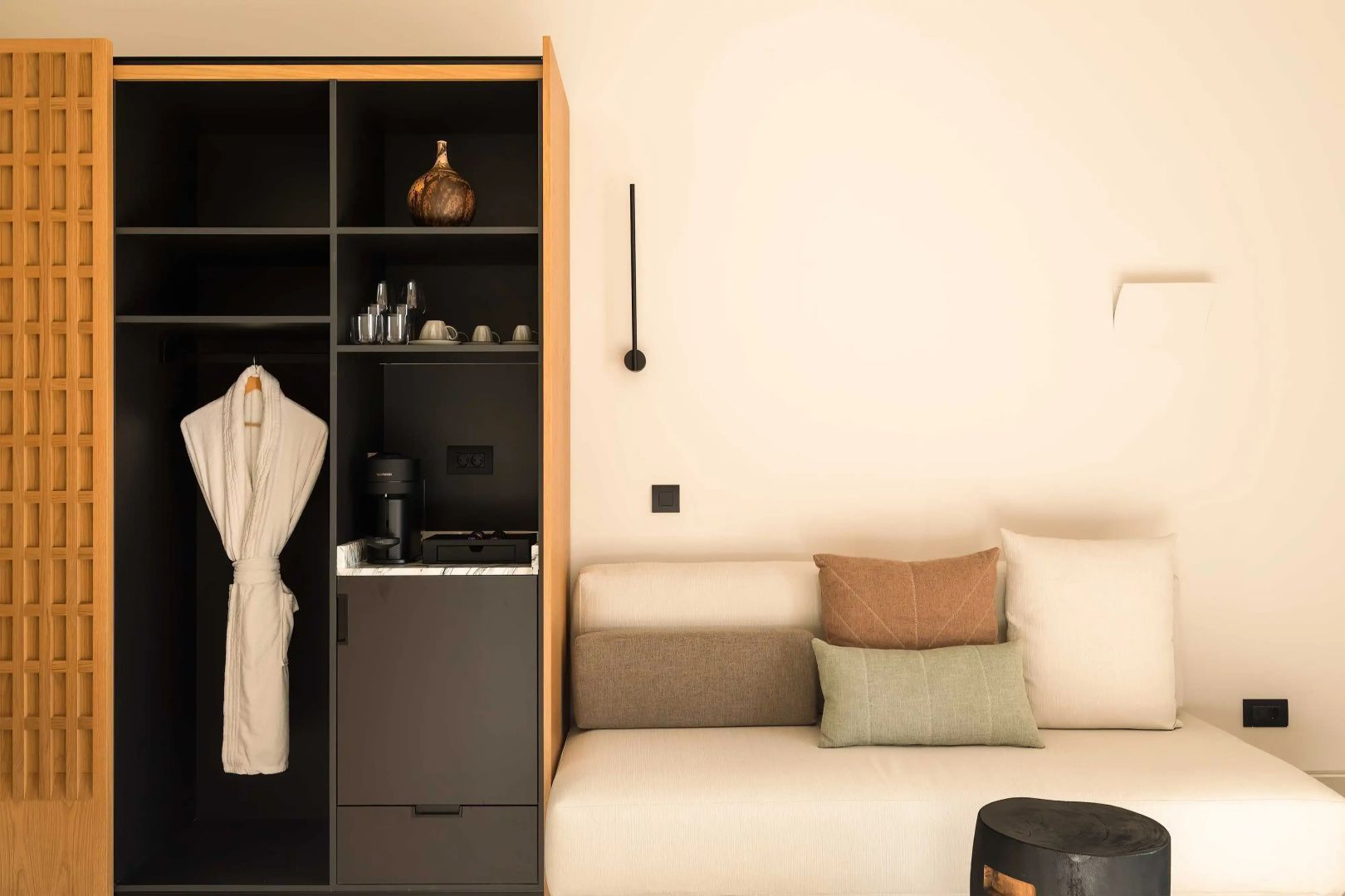 Sitzbereich im Zimmer mit beigem Sofa, Kissen und offenem Schrank samt Bademantel.