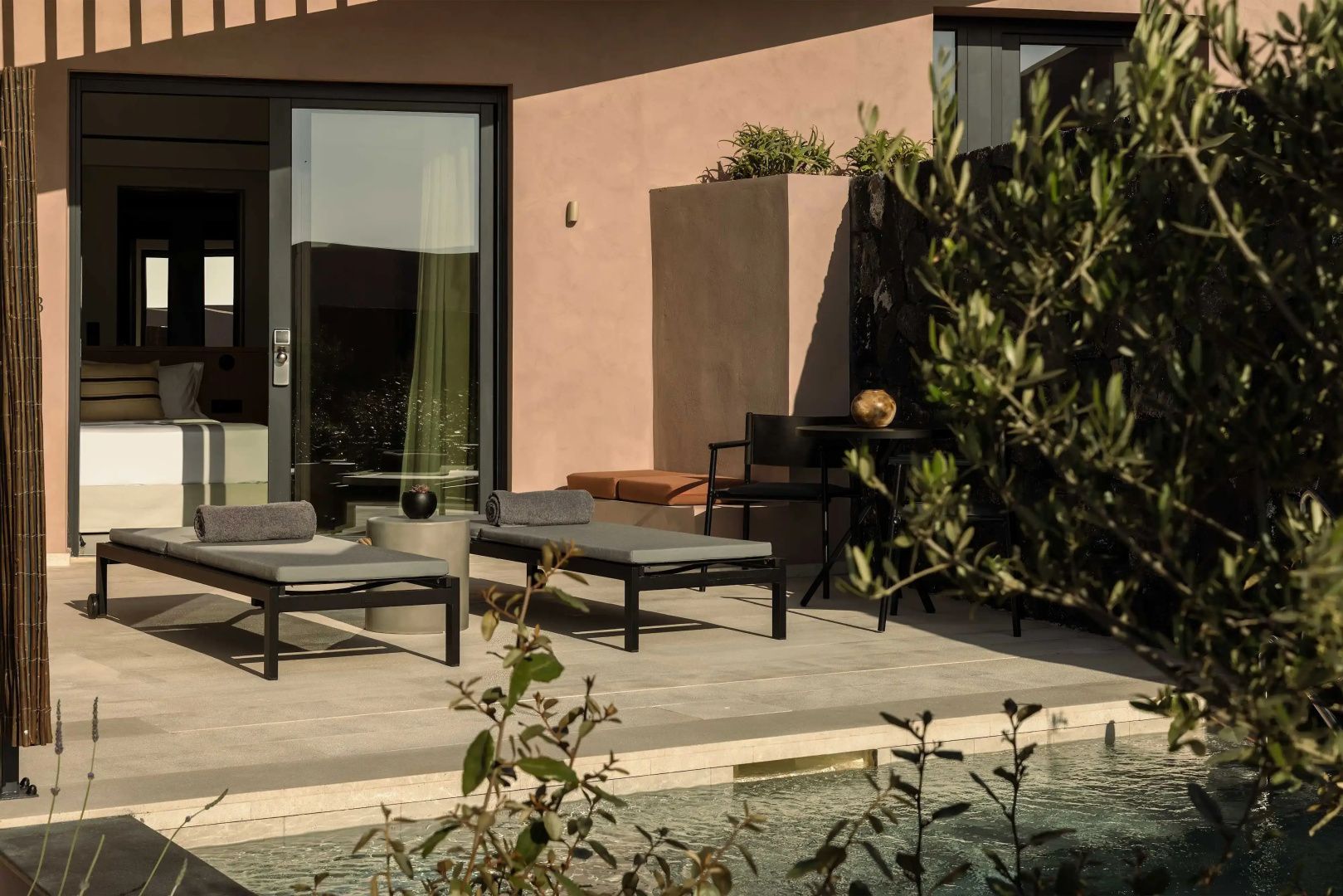 Privater Poolbereich mit zwei Sonnenliegen und einem Sitzbereich vor der Zimmerfassade.