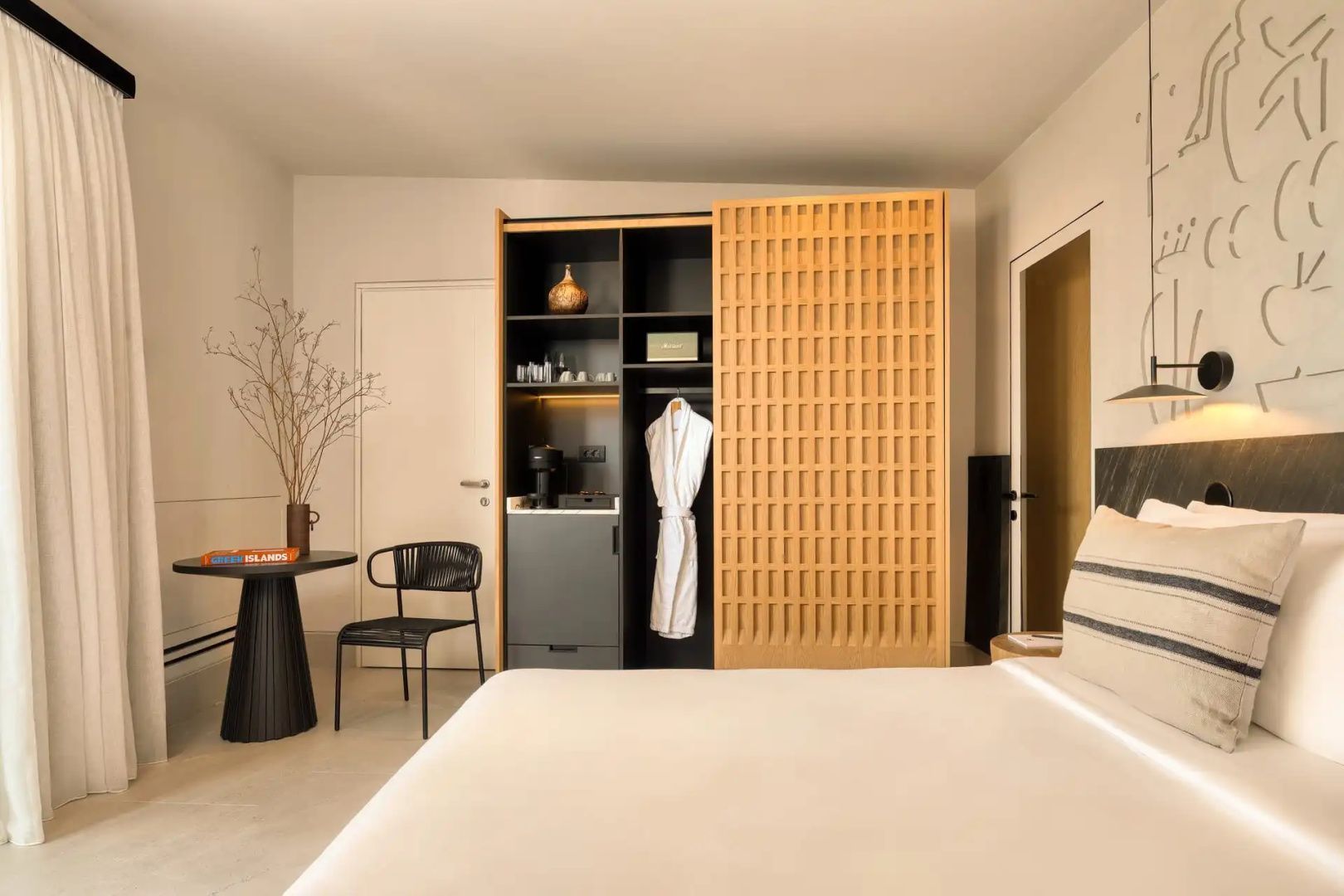 Hotelzimmer mit weißem Bett, Holzschrank mit Schiebetür sowie Tisch und Stuhl.