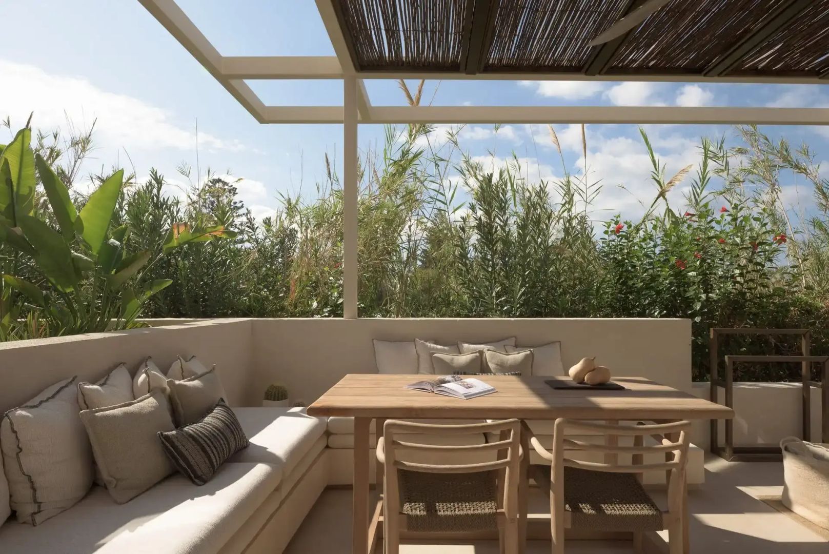 Überdachte Terrasse mit Esstisch aus Holz, Sitzbank und Blick ins Grüne.