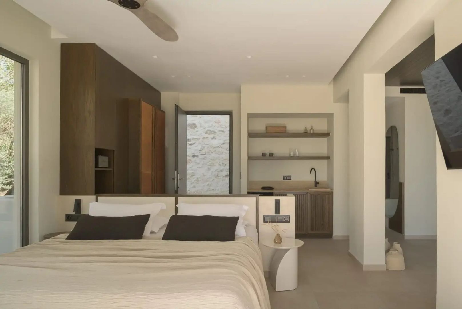 Modernes Schlafzimmer mit Doppelbett, hellen Wänden und einer Küchenzeile im Hintergrund.