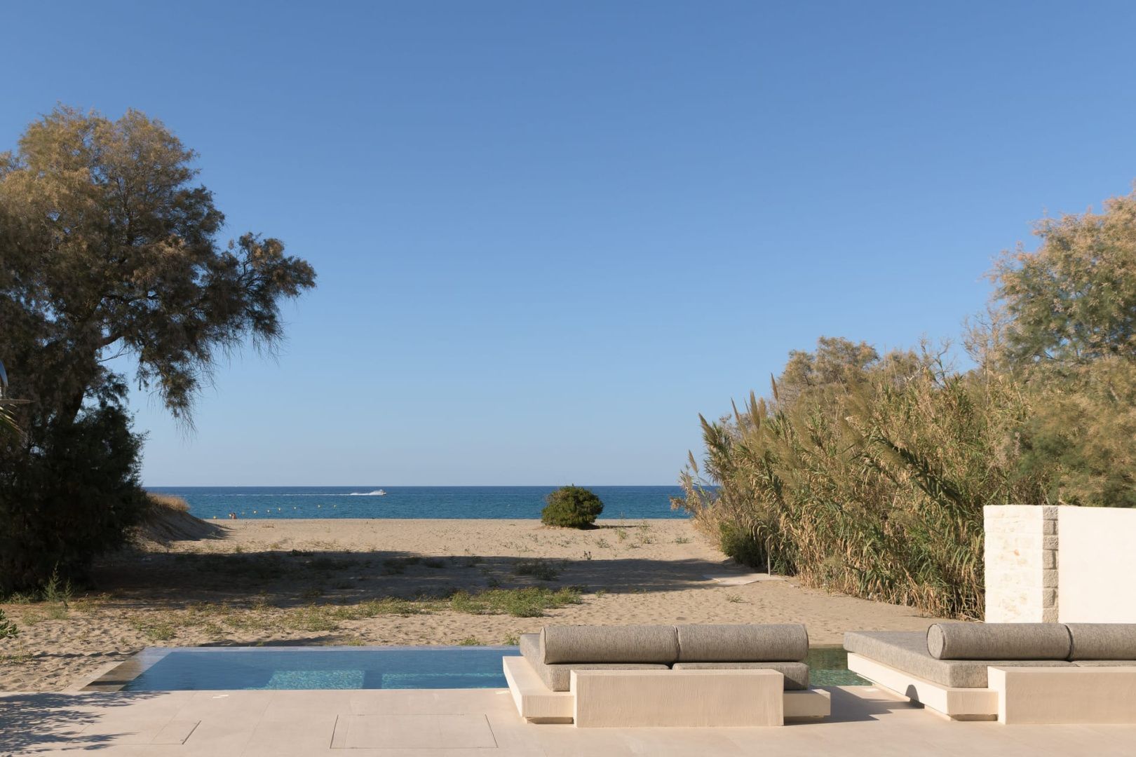 Blick von der Poolterrasse über den Sandstrand auf das ruhige blaue Meer.