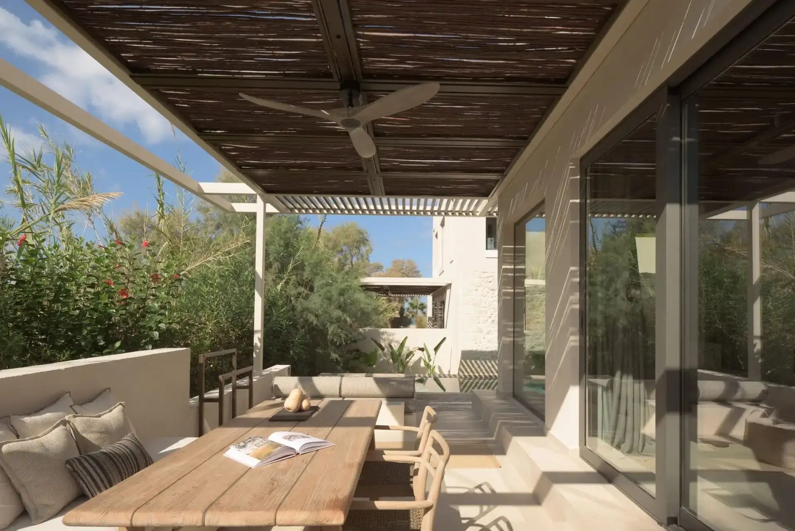 Terrassenbereich mit Holztisch, Stühlen und Reetdachabdeckung vor der Fassade.