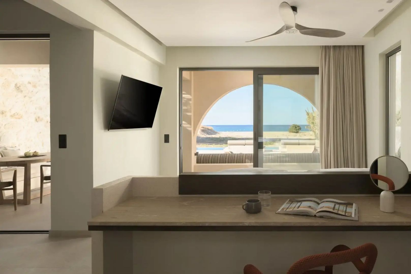 Blick aus dem hell eingerichteten Hotelzimmer durch die Glasfront auf das Meer.
