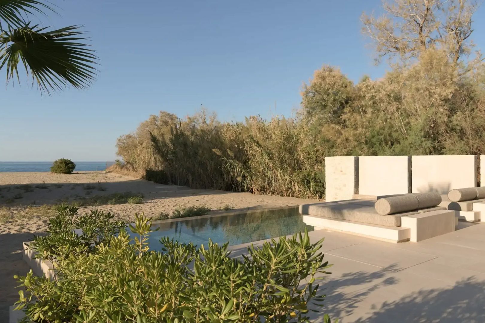 Terrassenbereich am Pool mit Liegebett, umgeben von grüner Vegetation nahe dem Strand.