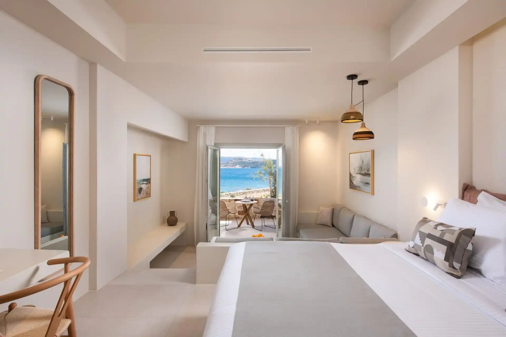 Helles Hotelzimmer mit Doppelbett, Sitzbereich und geöffneter Tür zur Terrasse mit Meerblick.