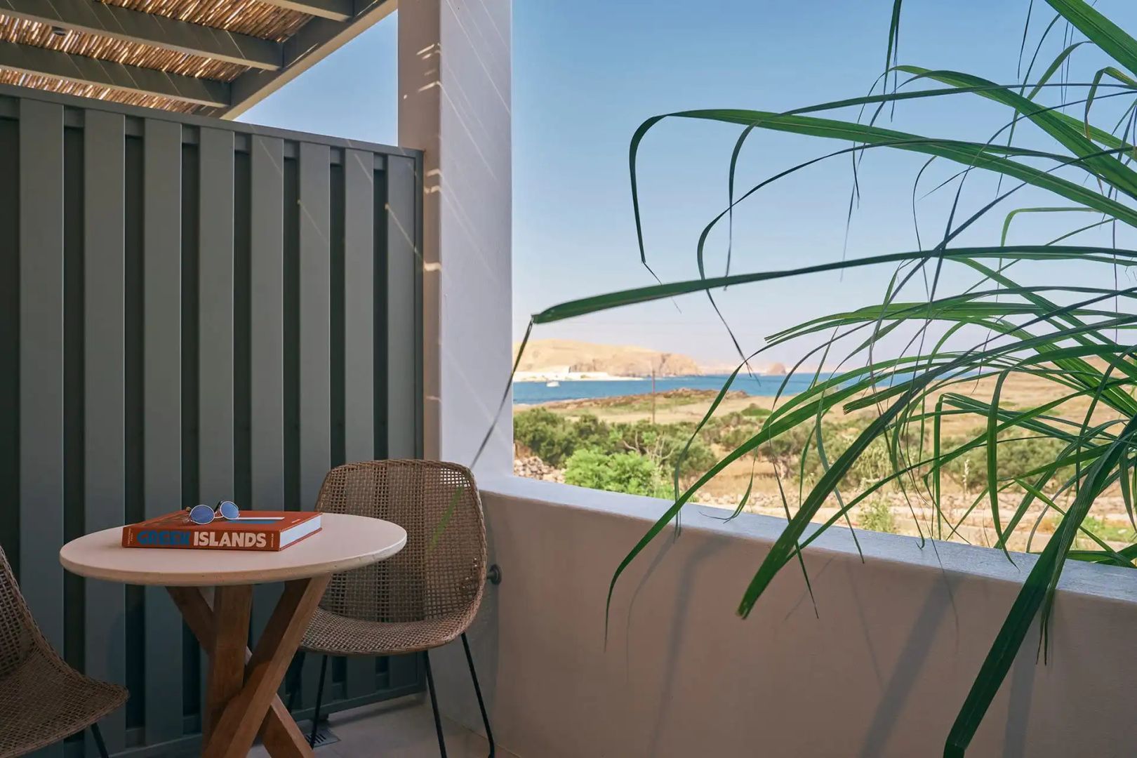 Balkon mit Stuhl und kleinem Tisch sowie Blick auf die umliegende Küstenlandschaft und das Meer.
