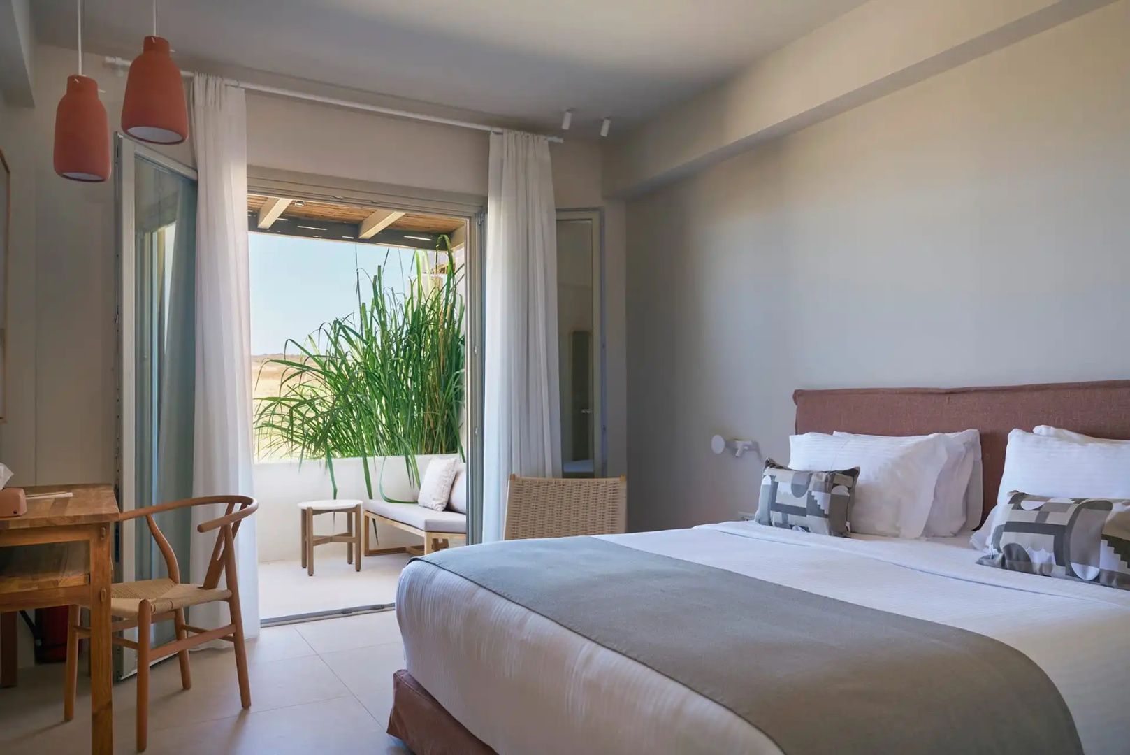 Hell eingerichtetes Schlafzimmer mit Doppelbett und Zugang zu einer bepflanzten Terrasse.