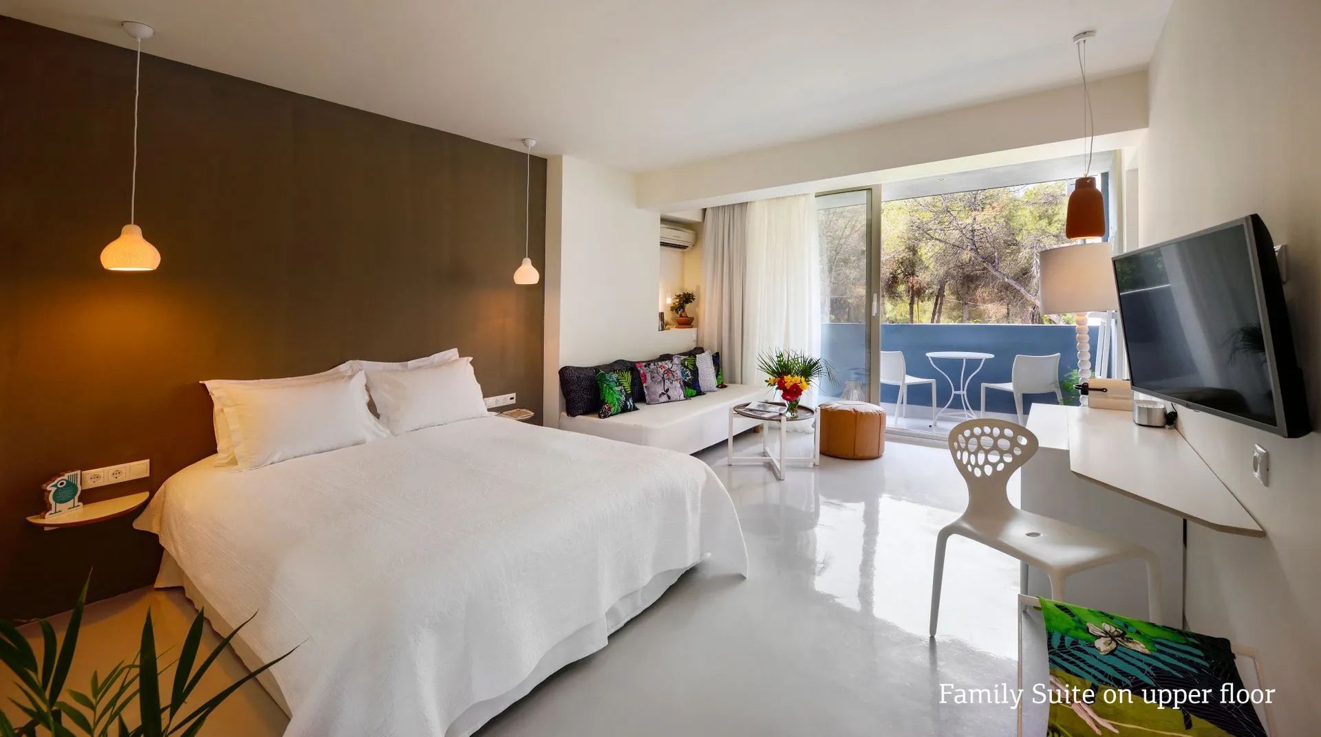 Helles Hotelzimmer mit Doppelbett, weißer Couch und verglastem Zugang zum Balkon.
